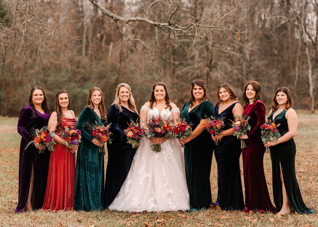 Courtney & John's bridal party lines up in jewel-toned velvet with bright winter bouquets at Covey Creek.