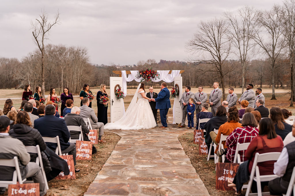 Courtney & John exchange vows at a flower-draped arbor as guests watch along the stone aisle at Covey Creek.