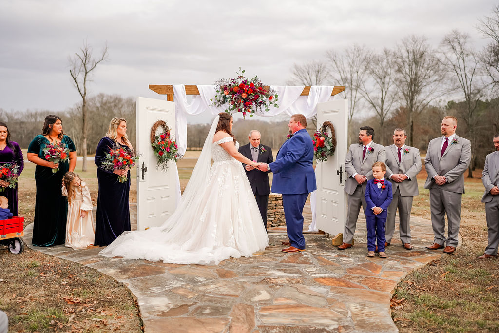 Courtney & John hold hands at the flower-draped arbor with their wedding party on the patio at Covey Creek.