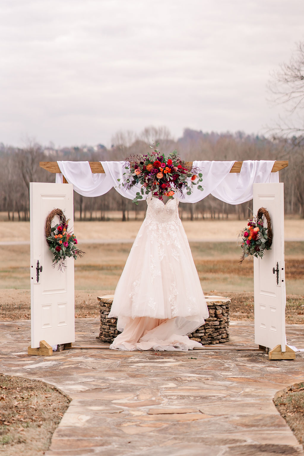 Courtney & John's lace gown hangs on a flower-draped arbor with white doors on the patio at Covey Creek.