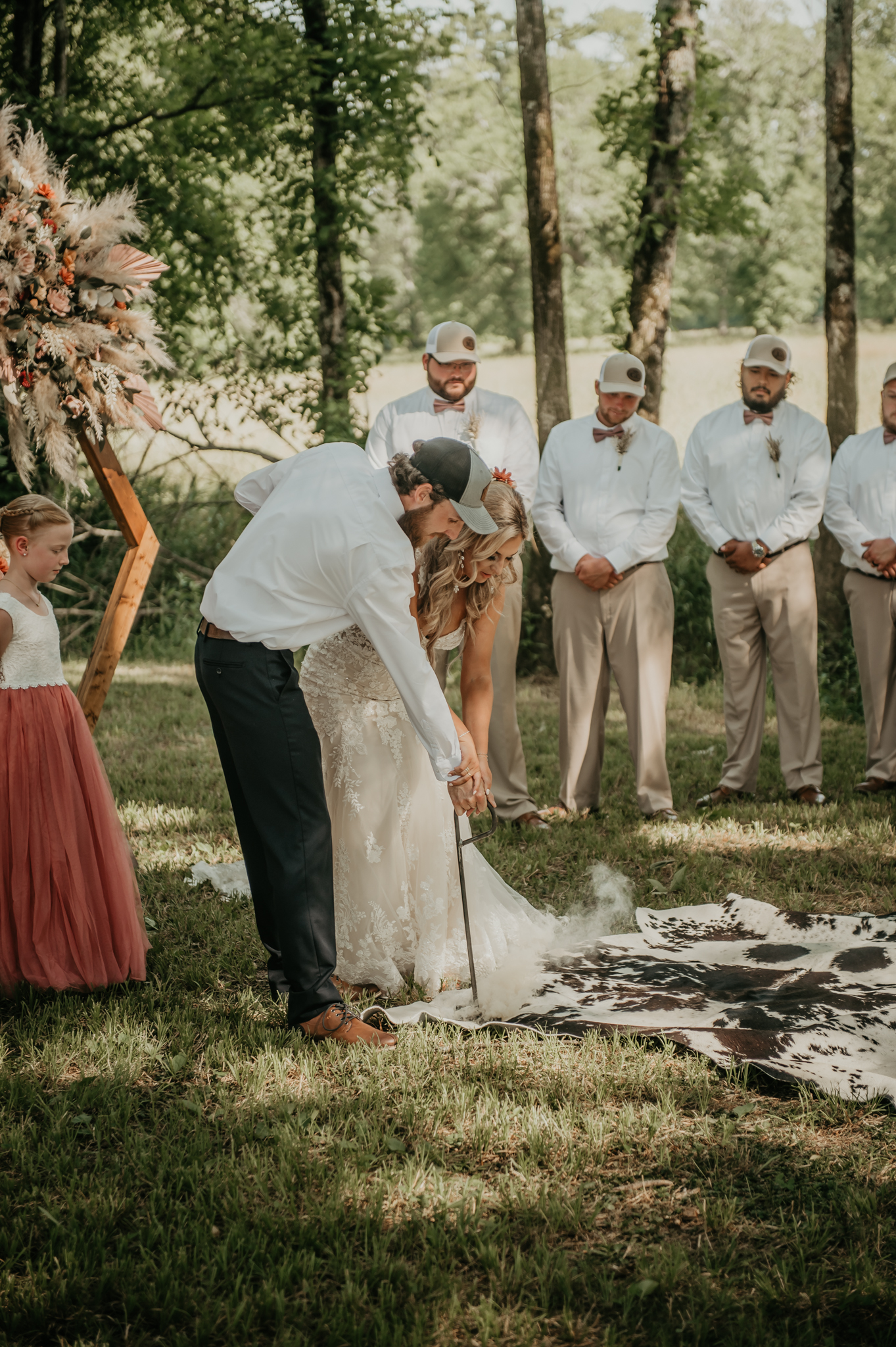 Hali & Kyle brand a cowhide rug at their Covey Creek ceremony as a flower girl and groomsmen look on.