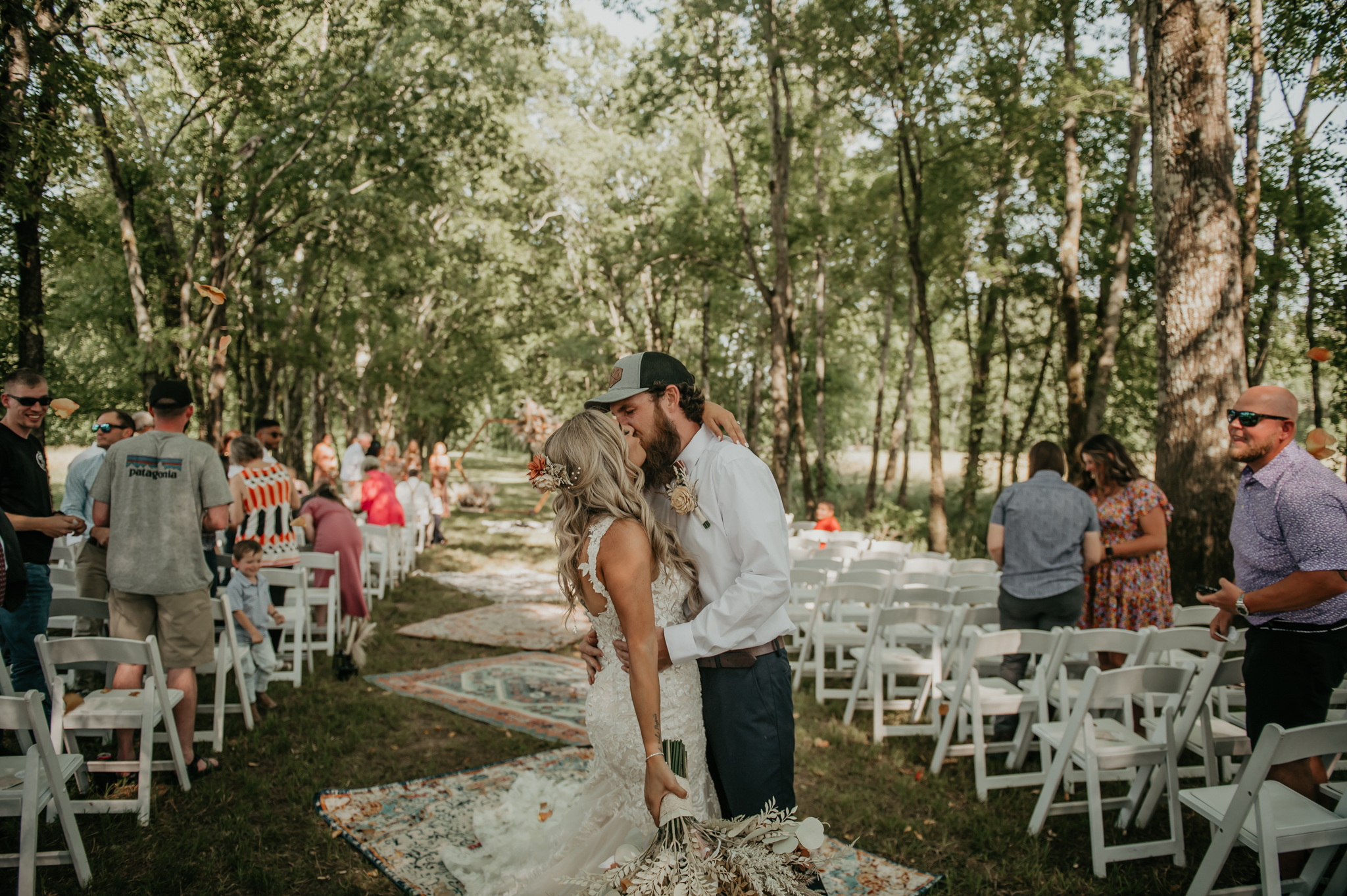Hali & Kyle share a kiss on the bohemian rug aisle at their wooded outdoor ceremony at Covey Creek.