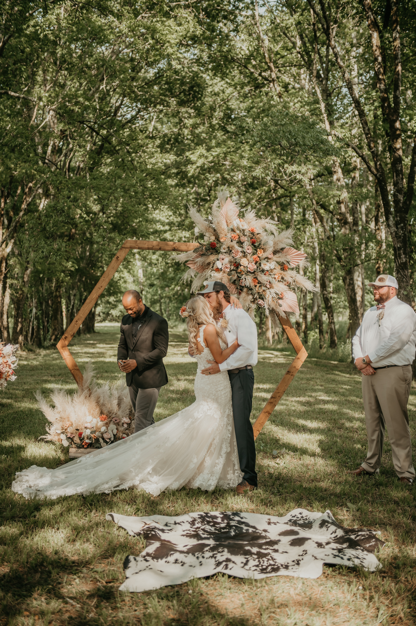 Hali & Kyle kiss at the floral hexagonal arbor during their wooded outdoor ceremony at Covey Creek.