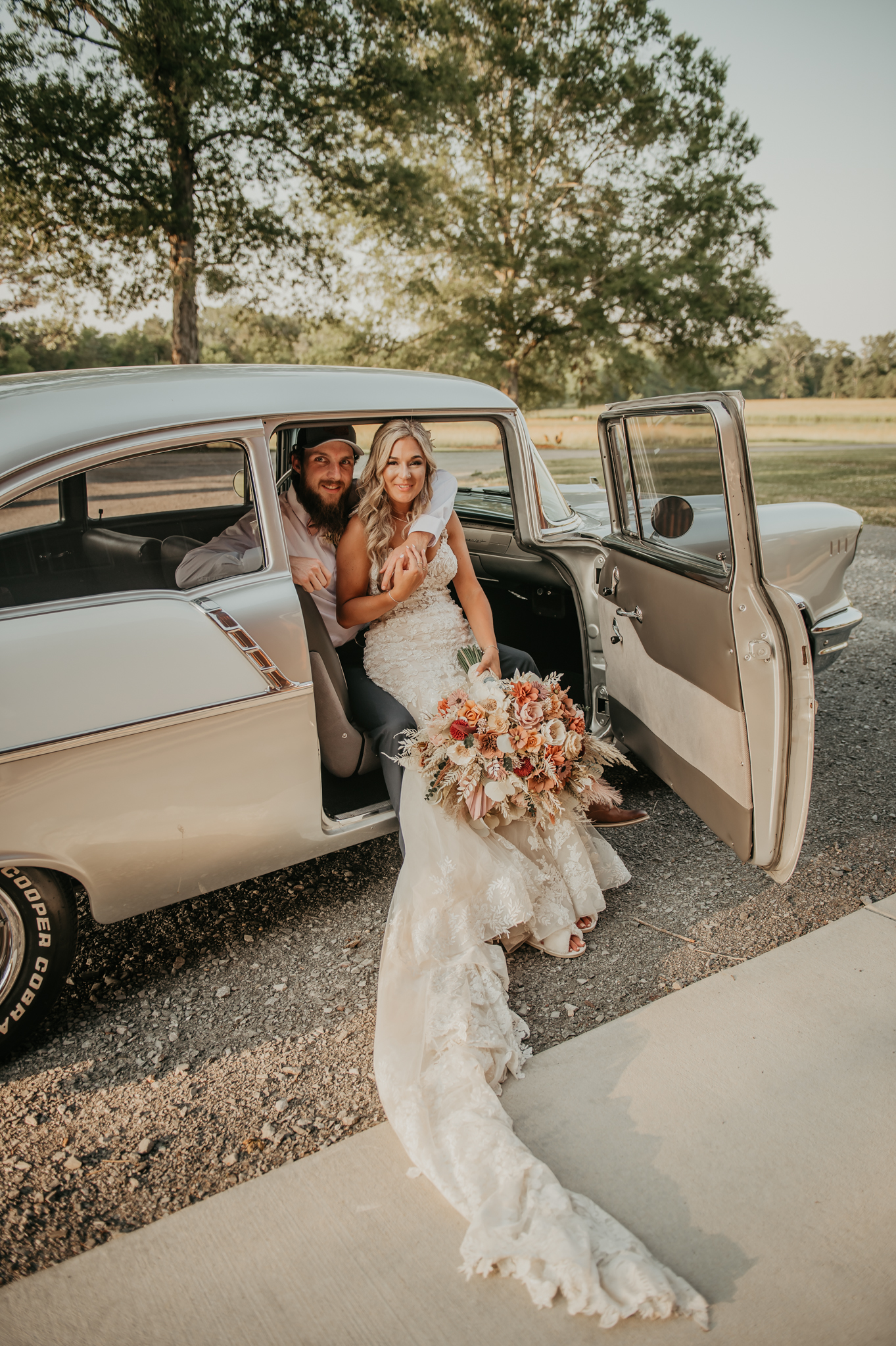 Hali & Kyle smile from a vintage Bel Air at Covey Creek, her lace train spilling onto the gravel.