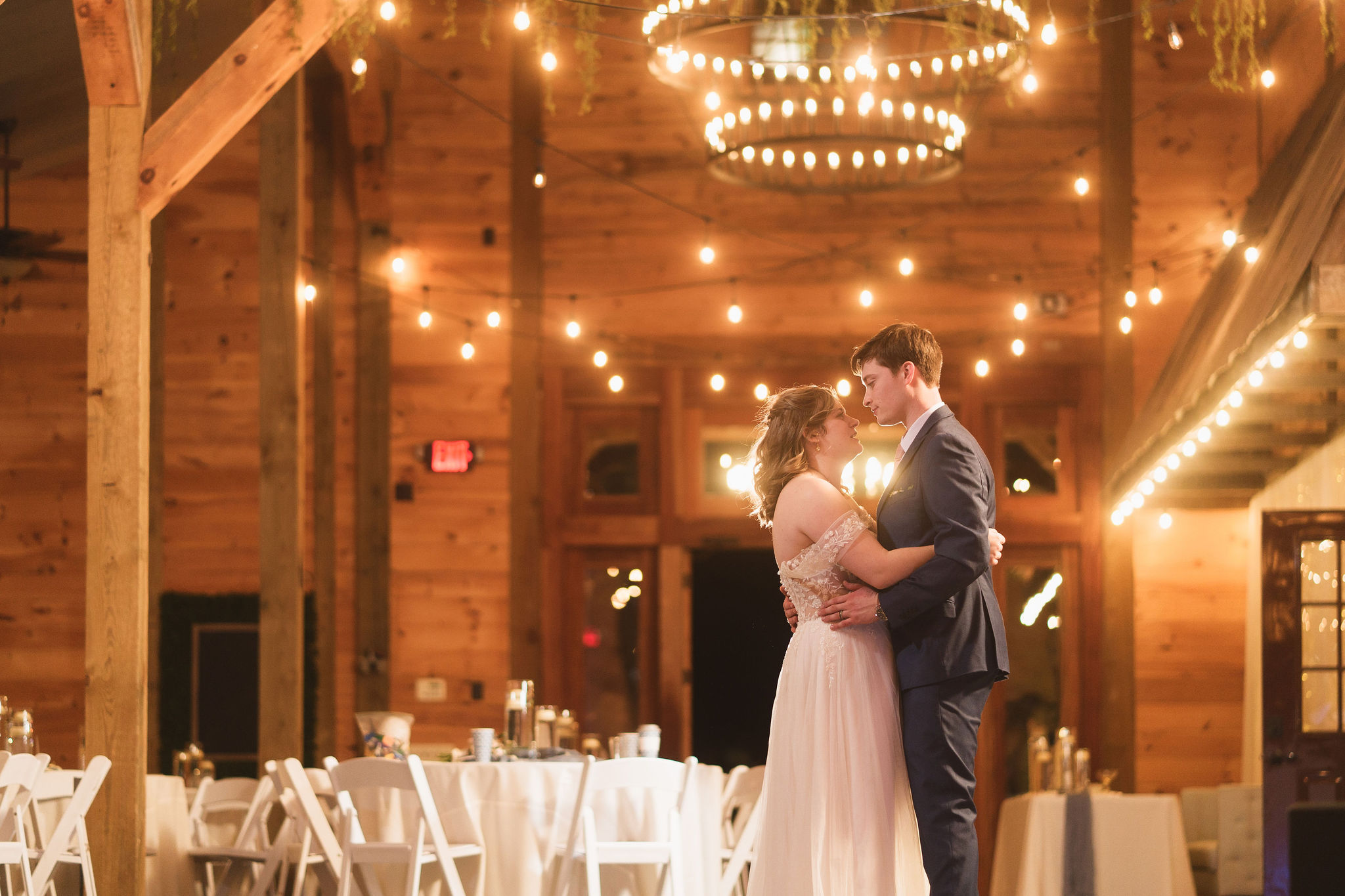 Ana & Carter share their first dance under string lights and a chandelier in the barn at Covey Creek