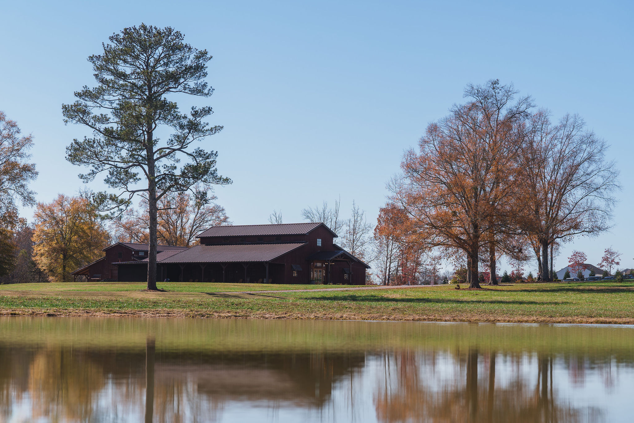 Ana & Carter wedding day view of the Covey Creek barn reflected in the still pond under clear blue sky