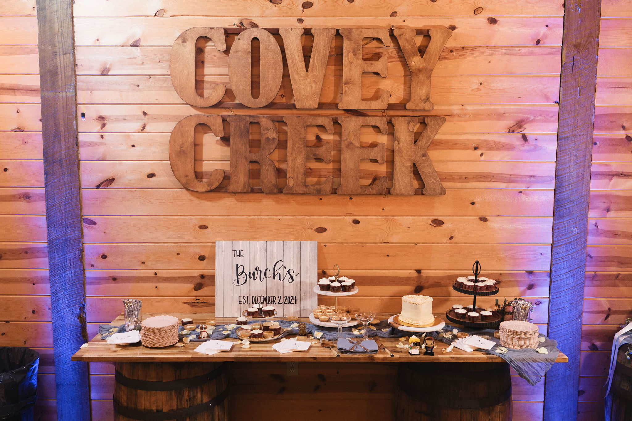 Ana & Carter dessert table on barrels under Covey Creek letters with cake, cupcakes, and Burch sign