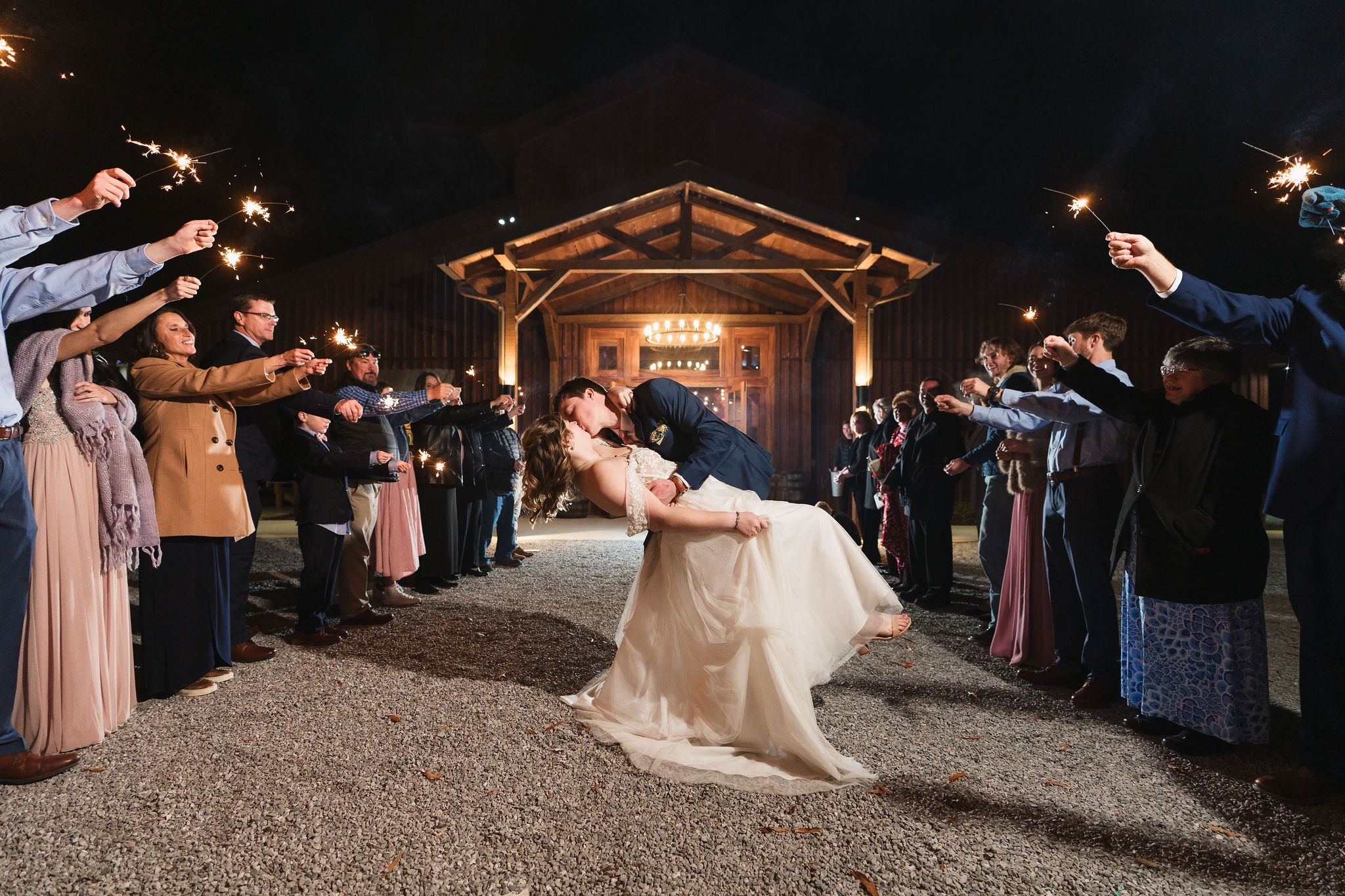 Ana & Carter share a sparkler send-off kiss on the gravel path before the lit barn at Covey Creek