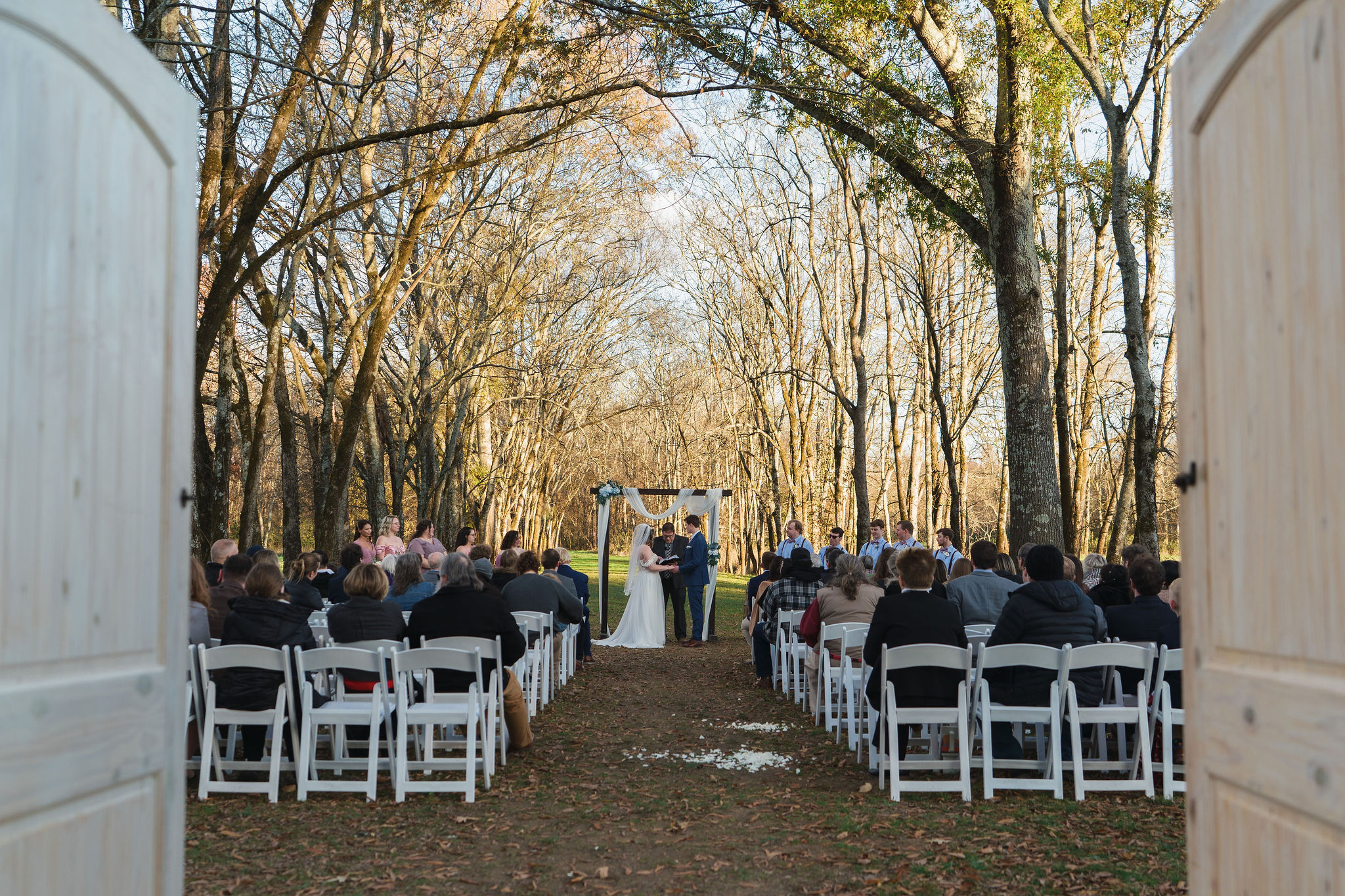 Ana & Carter exchange vows under a fabric-draped arch in the Tunnel of Love tree grove at Covey Creek