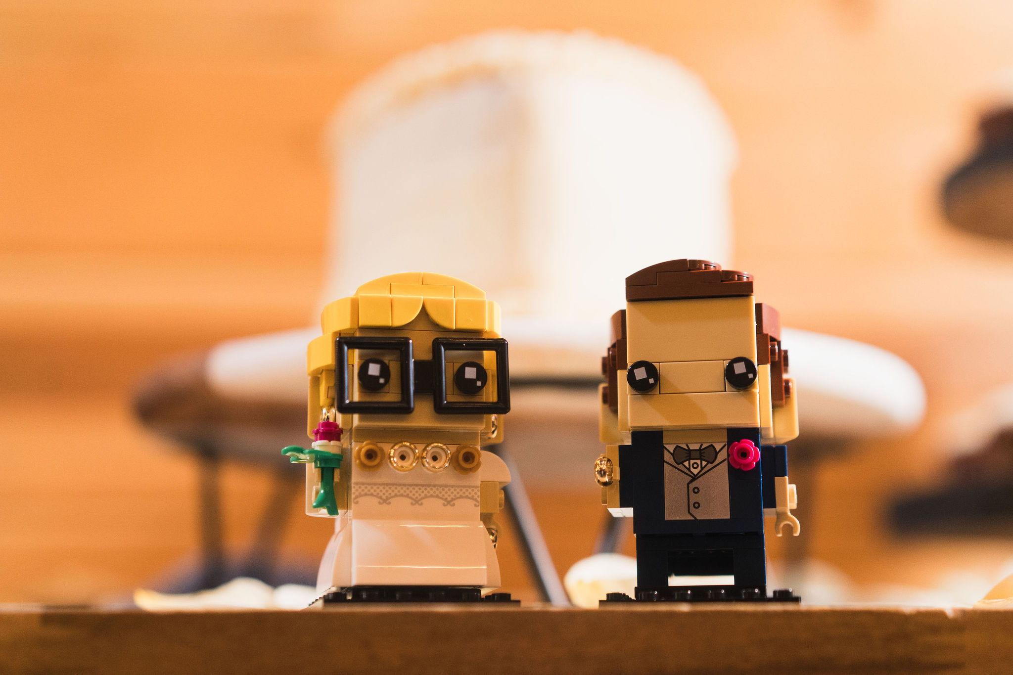 Ana & Carter LEGO-style bride and groom cake toppers on wood before a blurred cake at Covey Creek