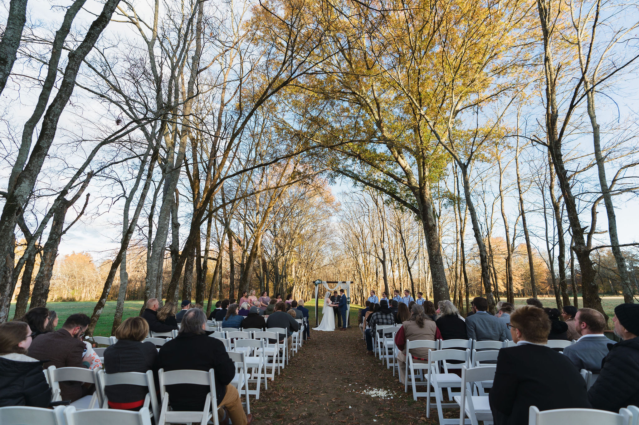 Ana & Carter stand at the altar under white fabric in the Tunnel of Love tree canopy at Covey Creek
