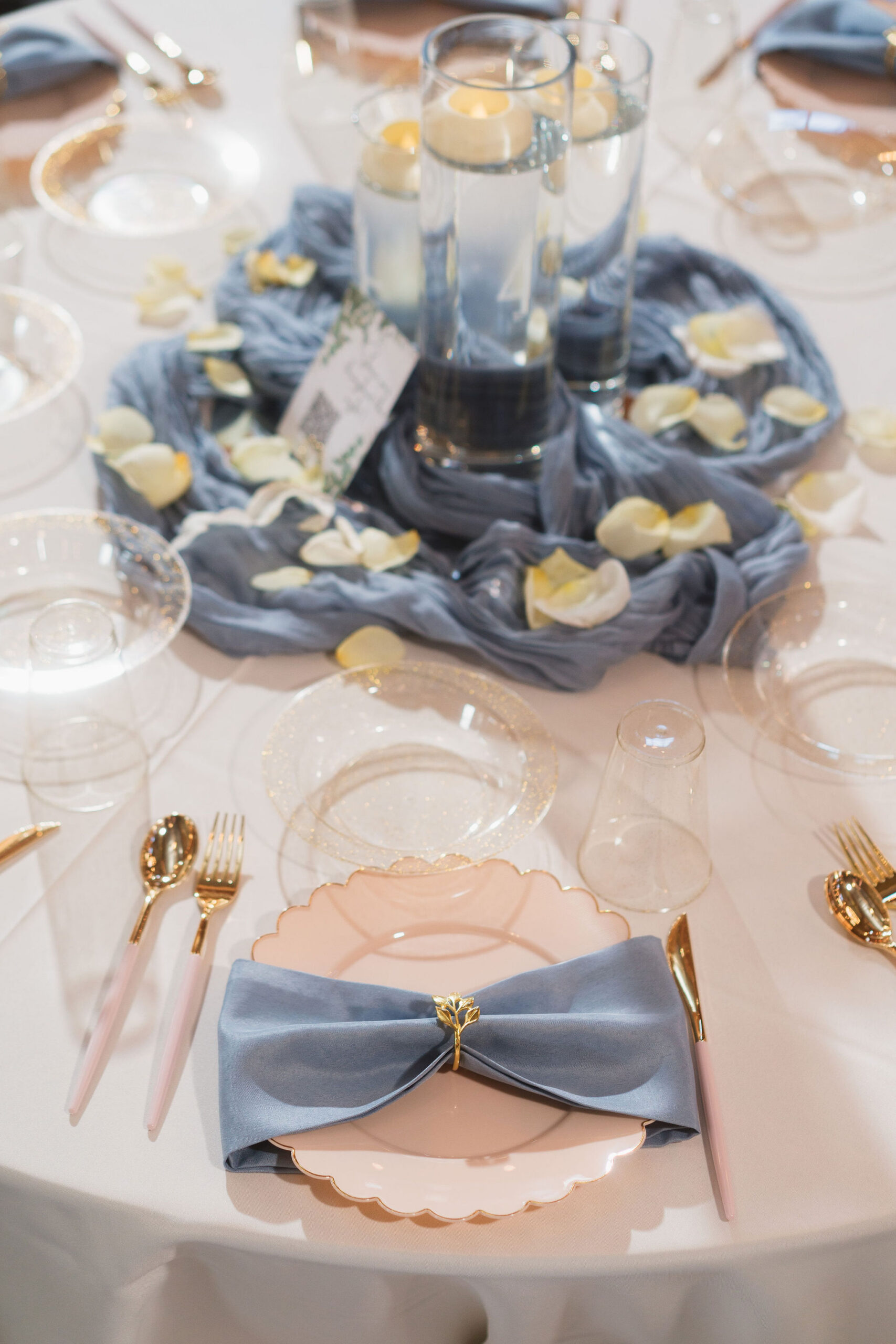 Ana & Carter place setting with dusty blue napkin bow, gold flatware, and floating candles at Covey Creek