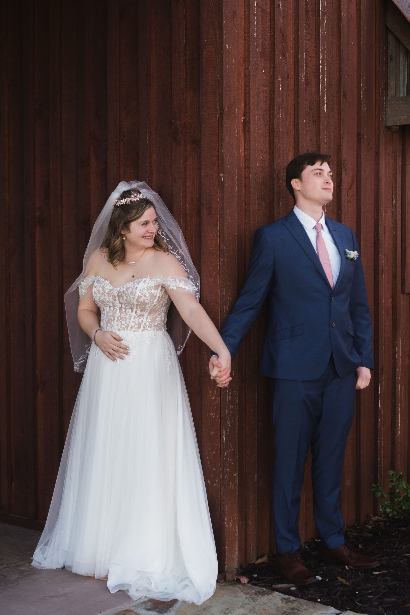 Ana & Carter hold hands around a barn corner for a first-look moment on the patio at Covey Creek