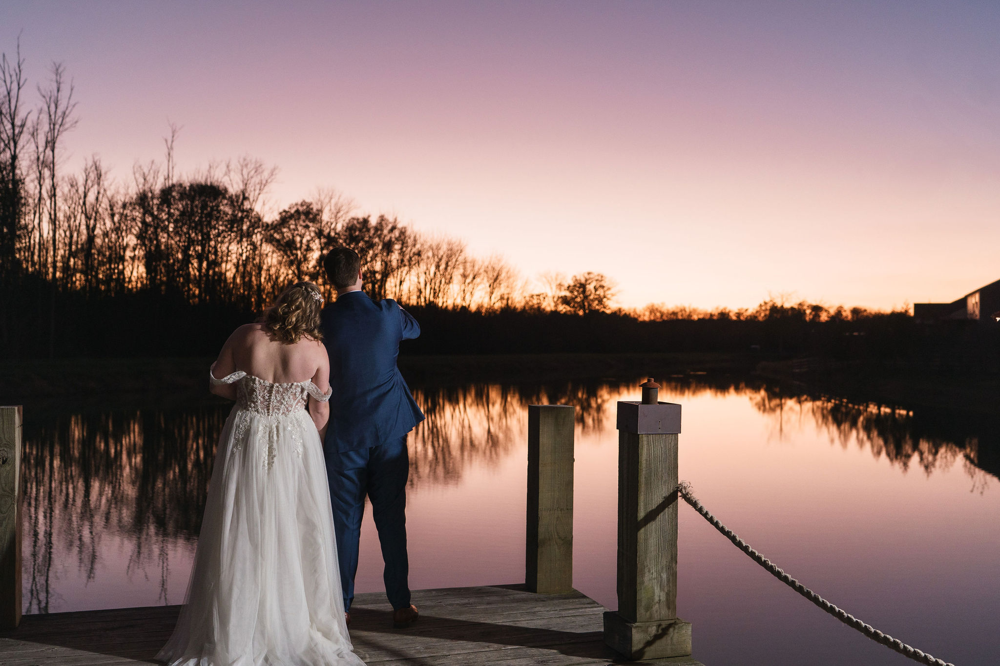 Ana & Carter stand on the Pond dock at sunset, her head on his shoulder over mirrored water at Covey Creek