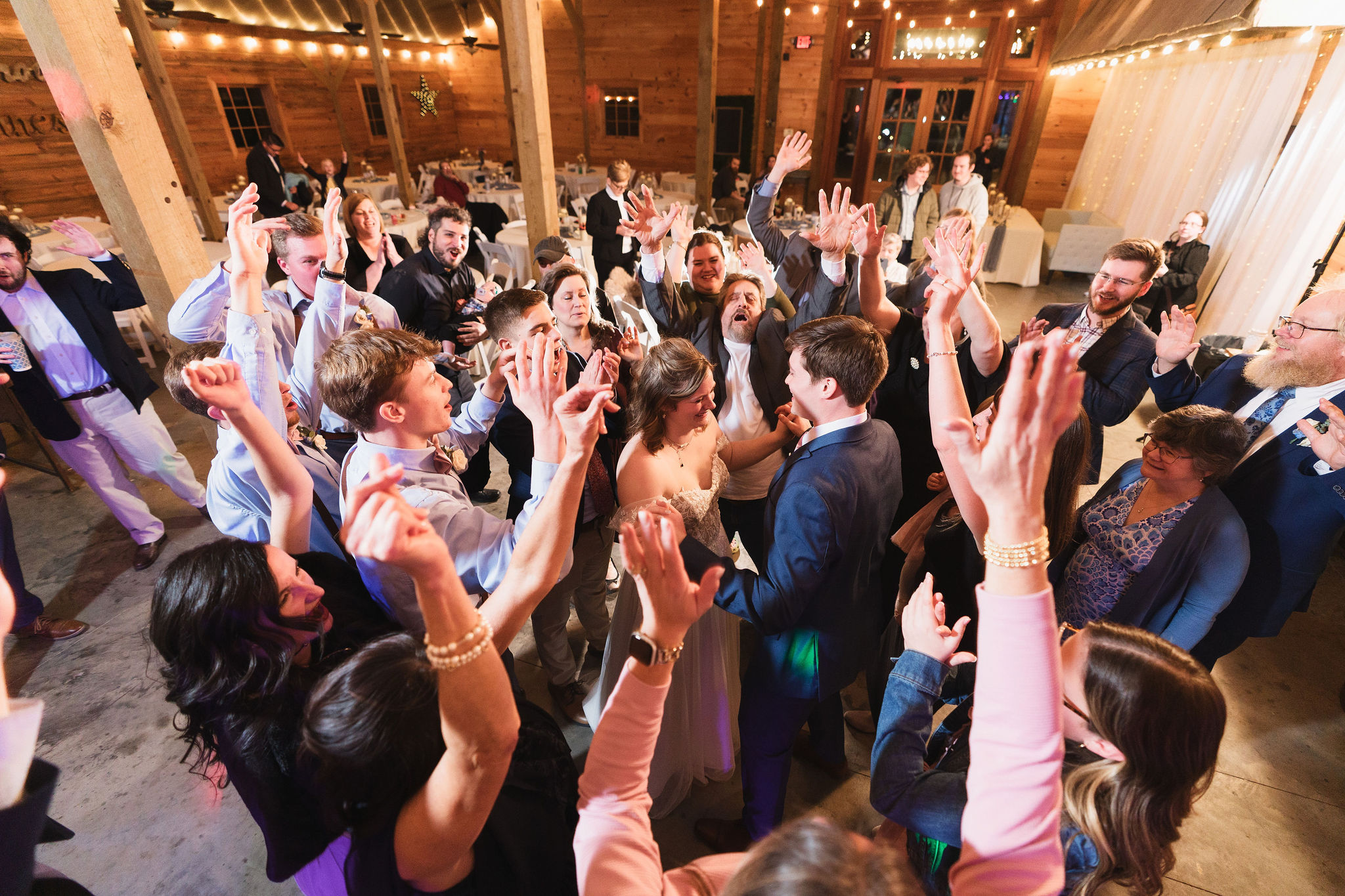 Ana & Carter celebrate on the barn dance floor as guests cheer in a circle around them at Covey Creek
