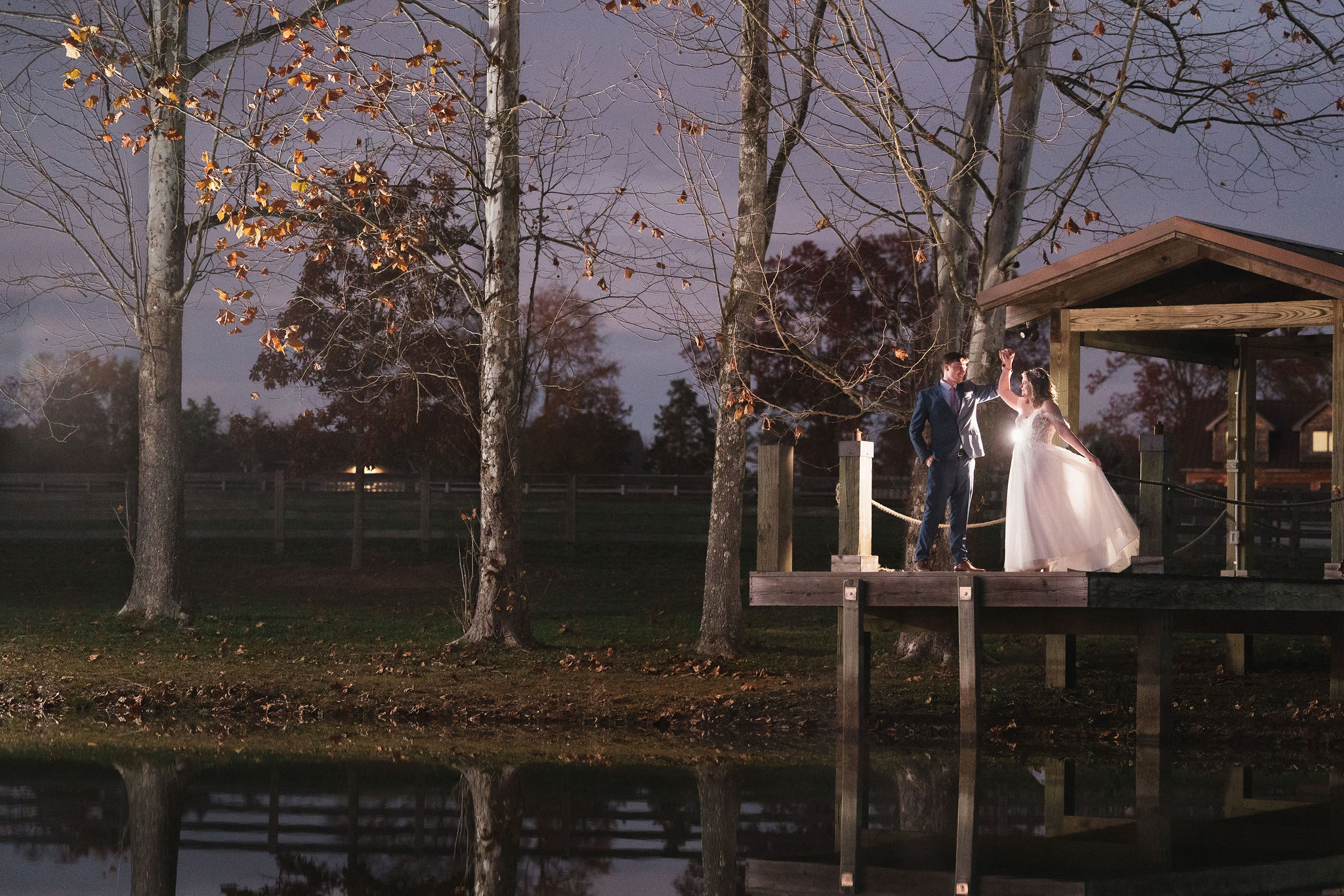 Ana & Carter twirl on the Pond dock at dusk with water reflections and autumn trees at Covey Creek