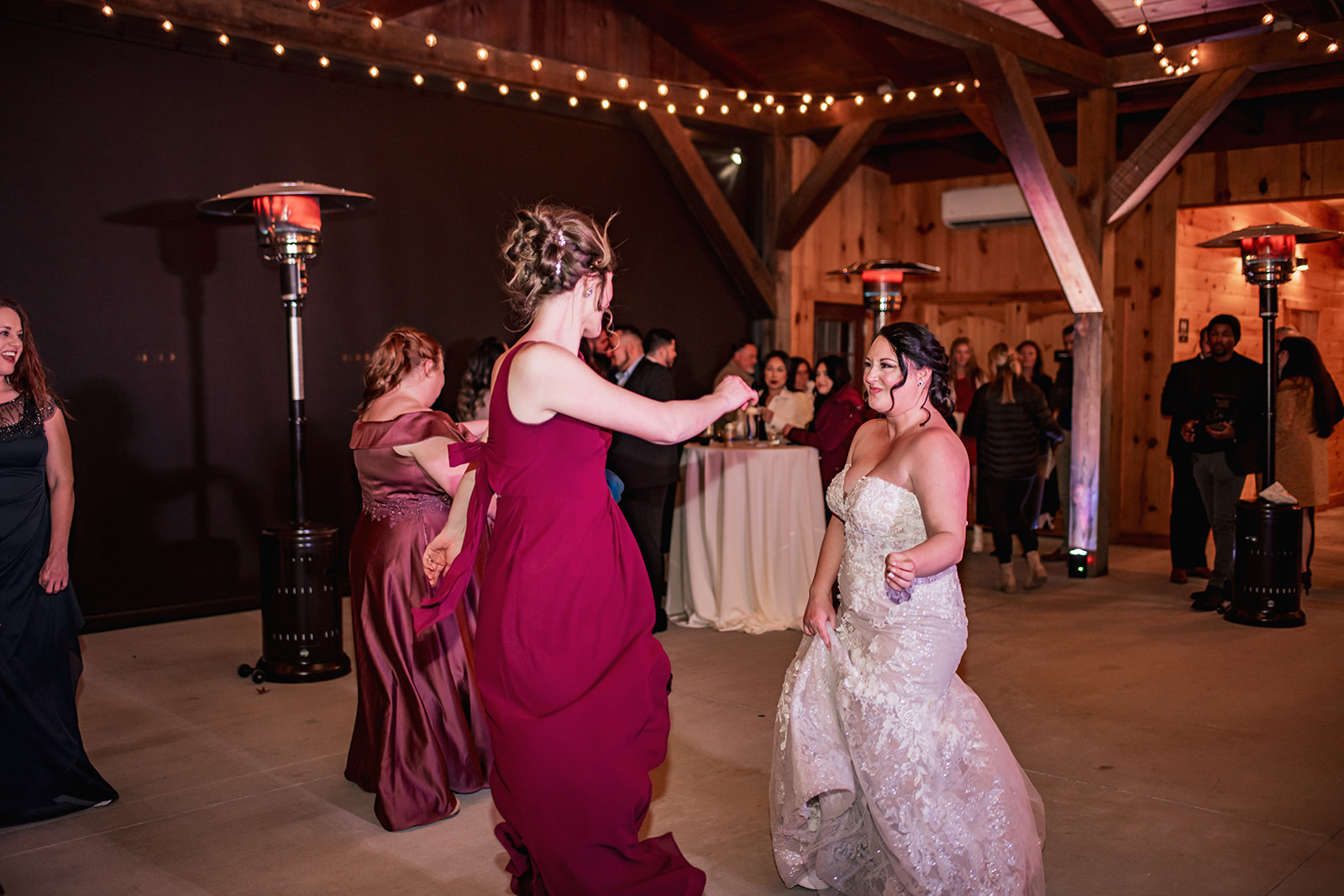 Annie dances with a burgundy-dressed bridesmaid under Covey Creek string lights and heaters at Annie & Will’s reception.