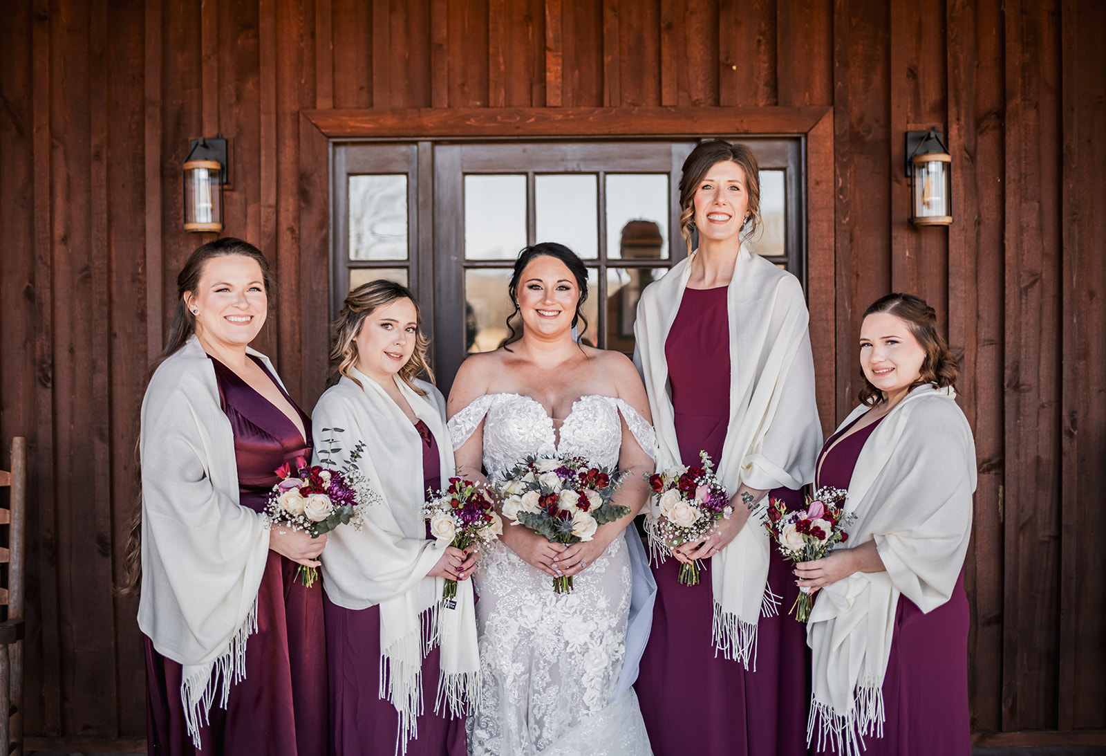 Annie & Will’s bridal party: Annie with burgundy-dressed bridesmaids in cream shawls before Covey Creek’s wood siding.
