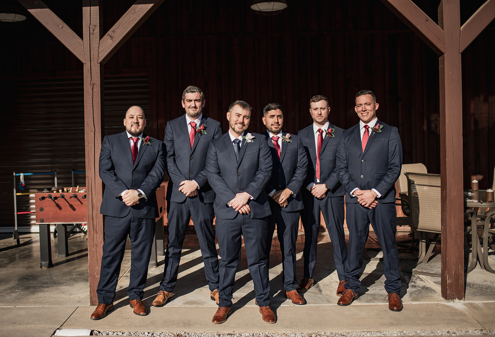 Will and navy-suited groomsmen in red ties pose under Covey Creek’s timber pavilion for Annie & Will’s wedding day.