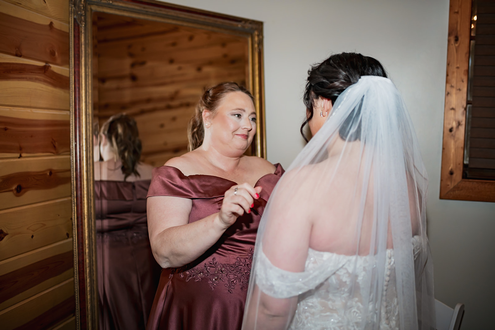 Annie’s mother adjusts her veil in a gold-framed mirror at Covey Creek before Annie & Will’s ceremony in wood-paneled walls.