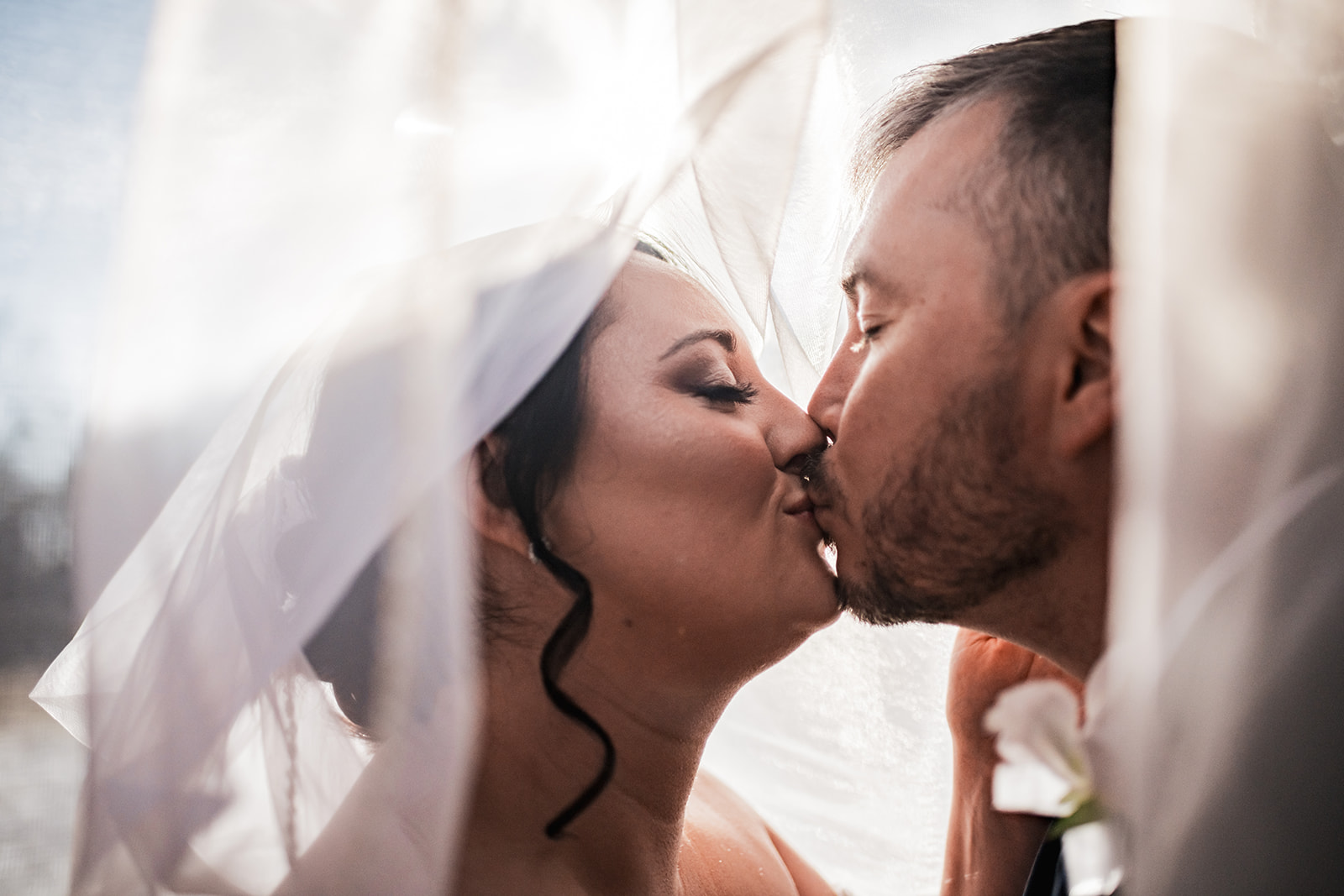 Annie & Will share a veiled kiss in soft backlight at Covey Creek, her updo and his white boutonniere caught in close profile.