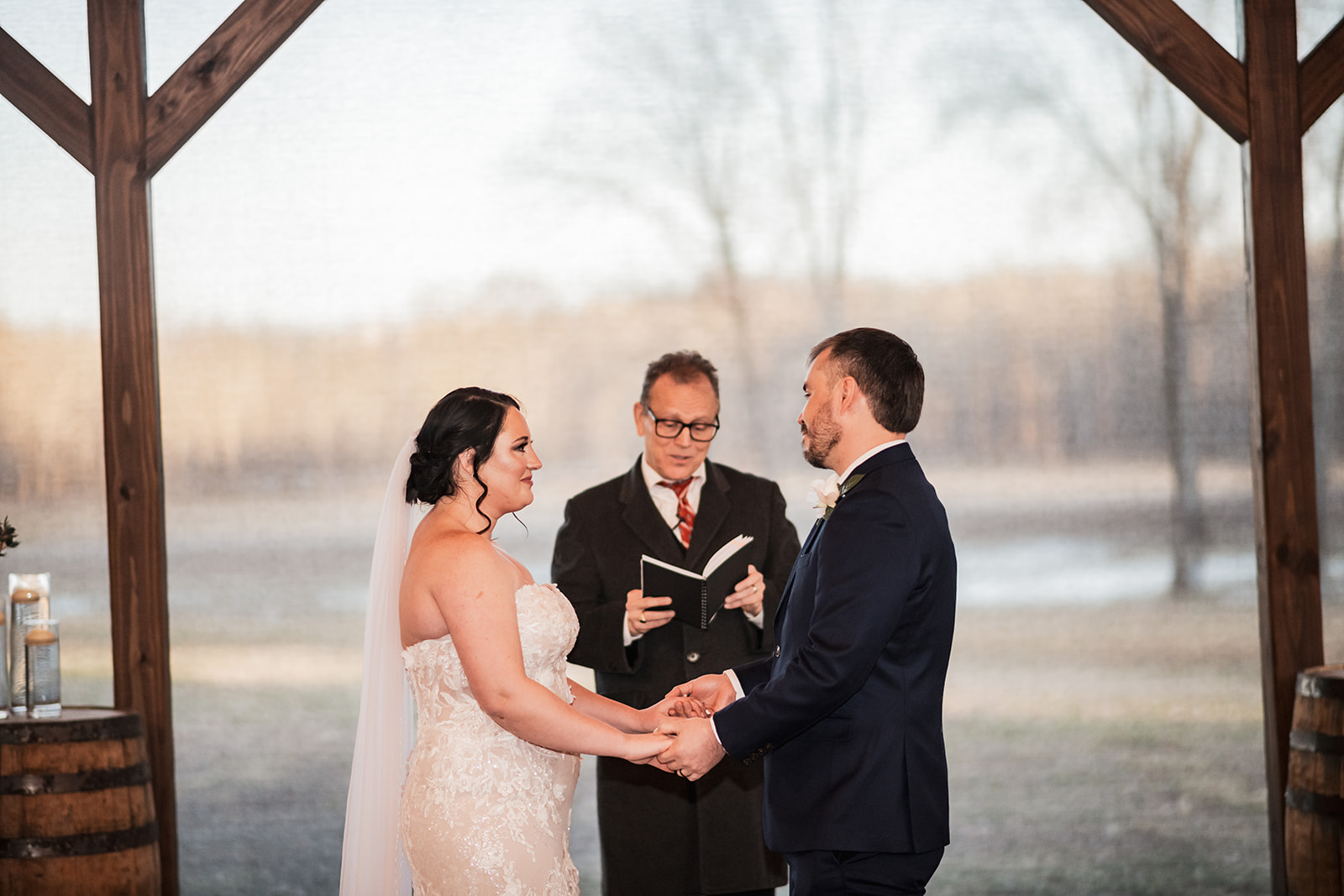Annie & Will hold hands exchanging vows under Covey Creek’s timber pavilion as the officiant reads between them.