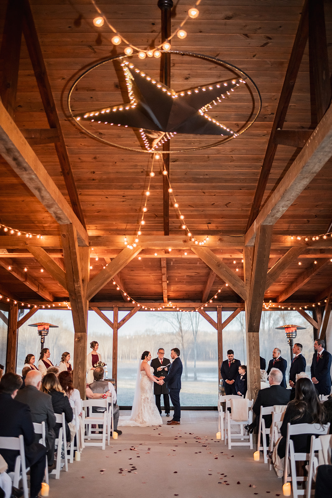 Annie & Will exchange vows under Covey Creek’s lit star in the timber pavilion as guests fill white chairs along the aisle.
