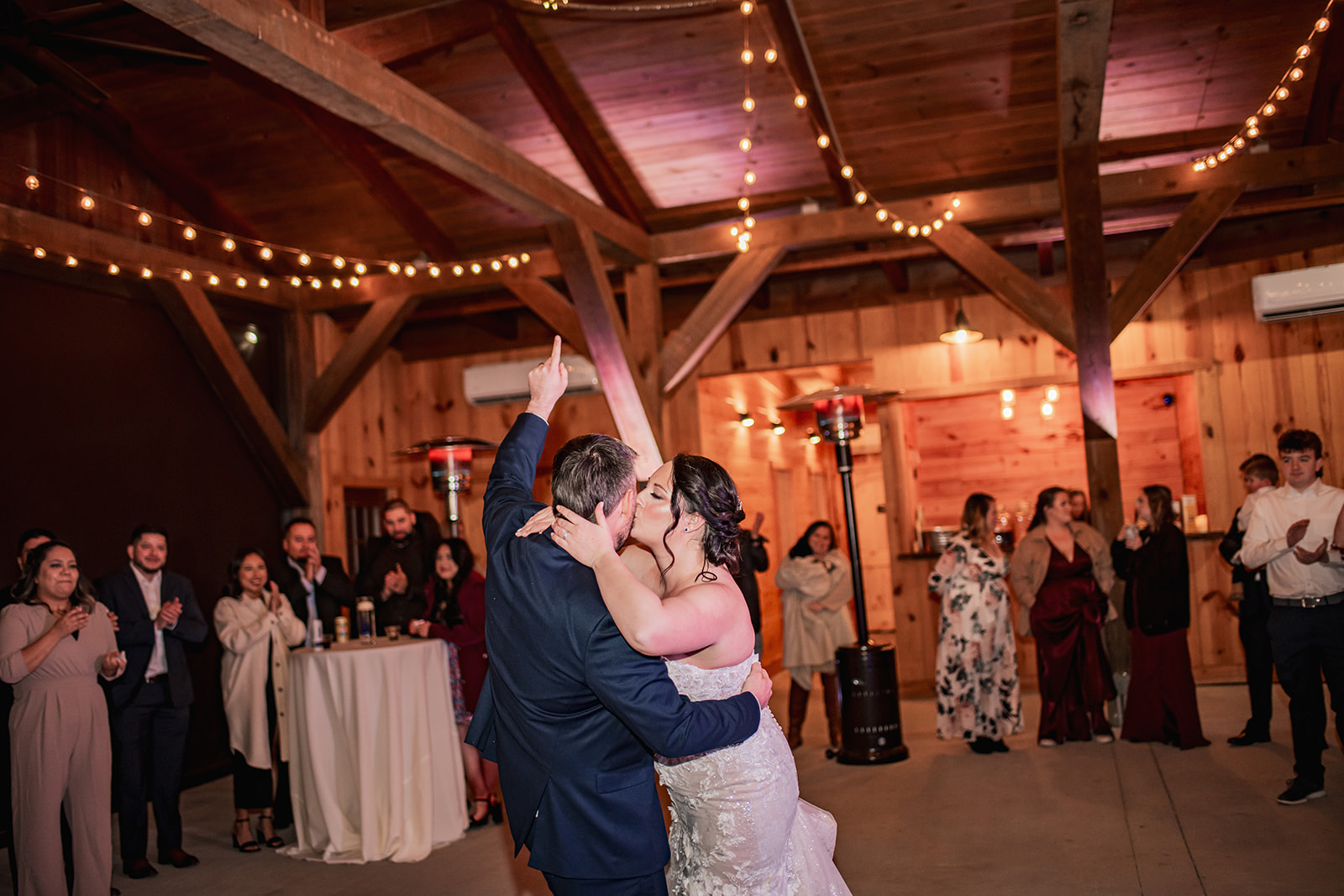 Annie & Will kiss on the Covey Creek dance floor as Will points skyward beneath warm Edison lights and timber beams.