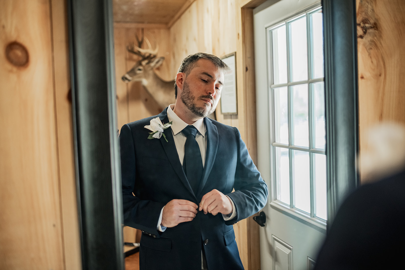 Will buttons his navy jacket in a wood-paneled Covey Creek suite with white boutonniere for Annie & Will’s wedding day.