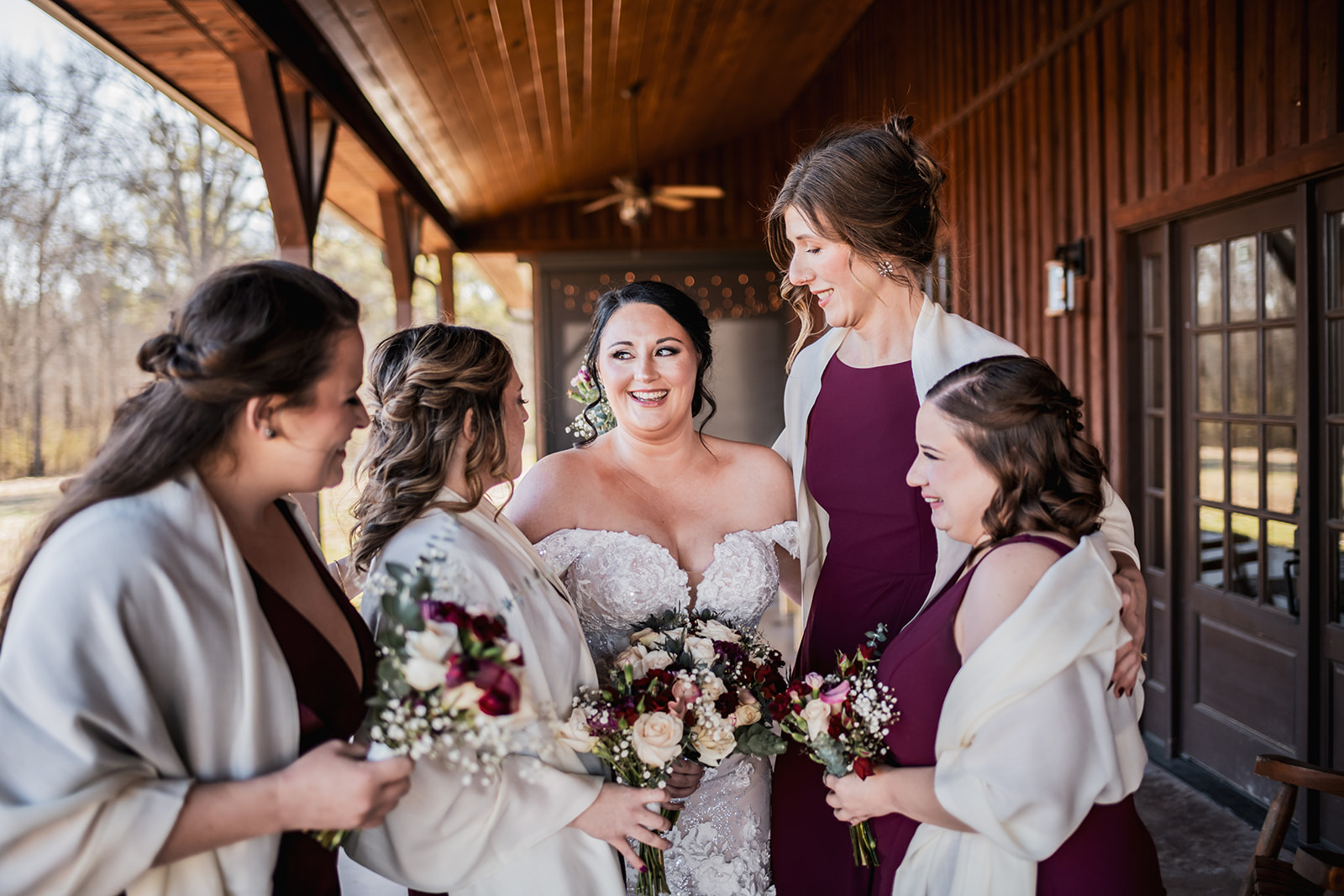 Annie laughs with burgundy bridesmaids in cream shawls on Covey Creek’s porch at Annie & Will’s wedding, rose bouquets in hand.