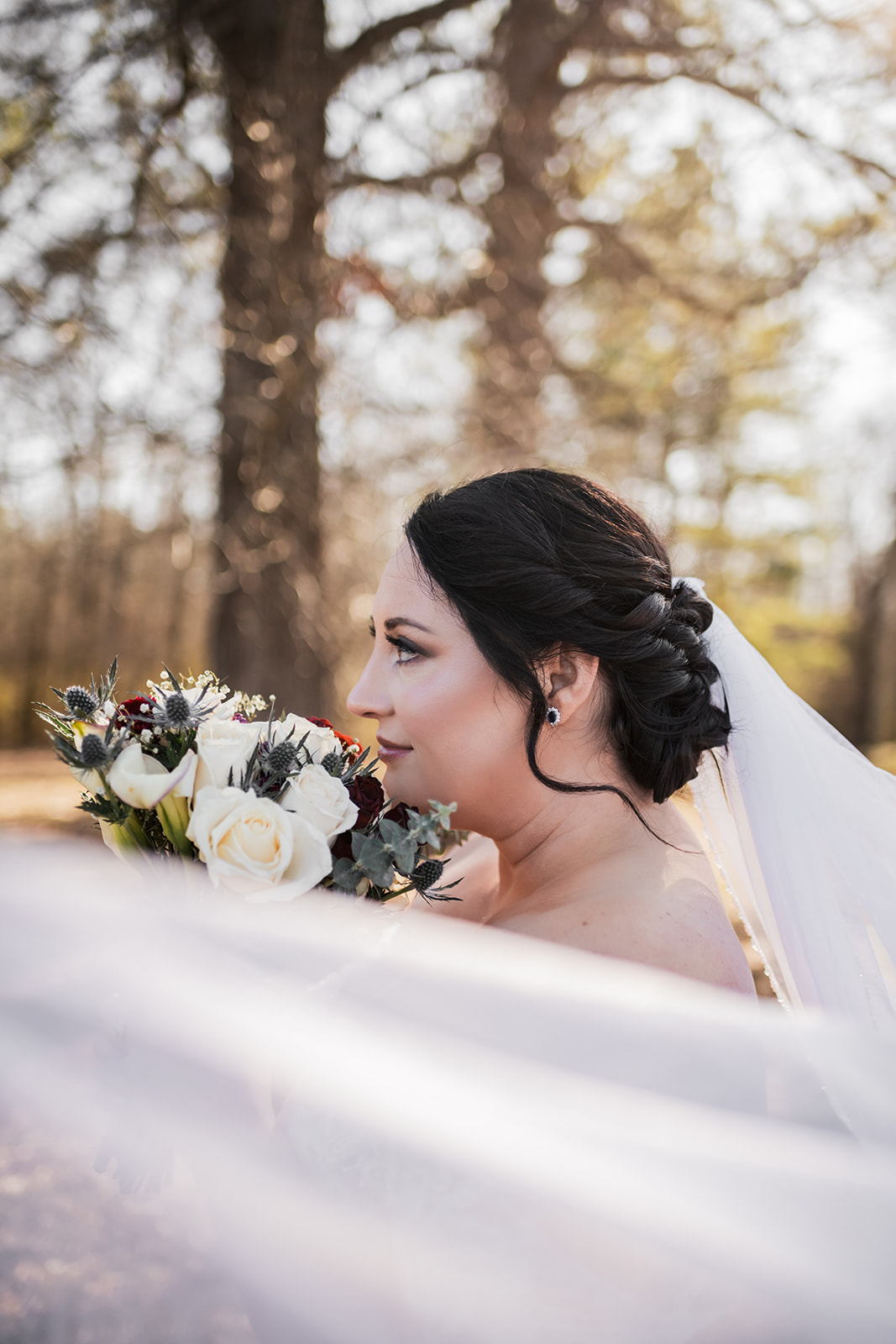 Annie holds white roses and blue thistle beside her flowing veil in golden woods at Covey Creek for Annie & Will’s day.