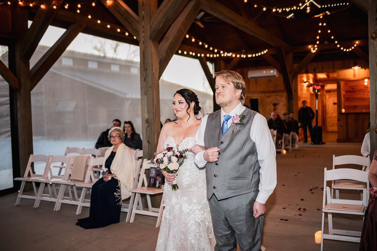 Annie & Will walk the petal-strewn aisle under Covey Creek string lights, guests seated on white chairs beside candles.