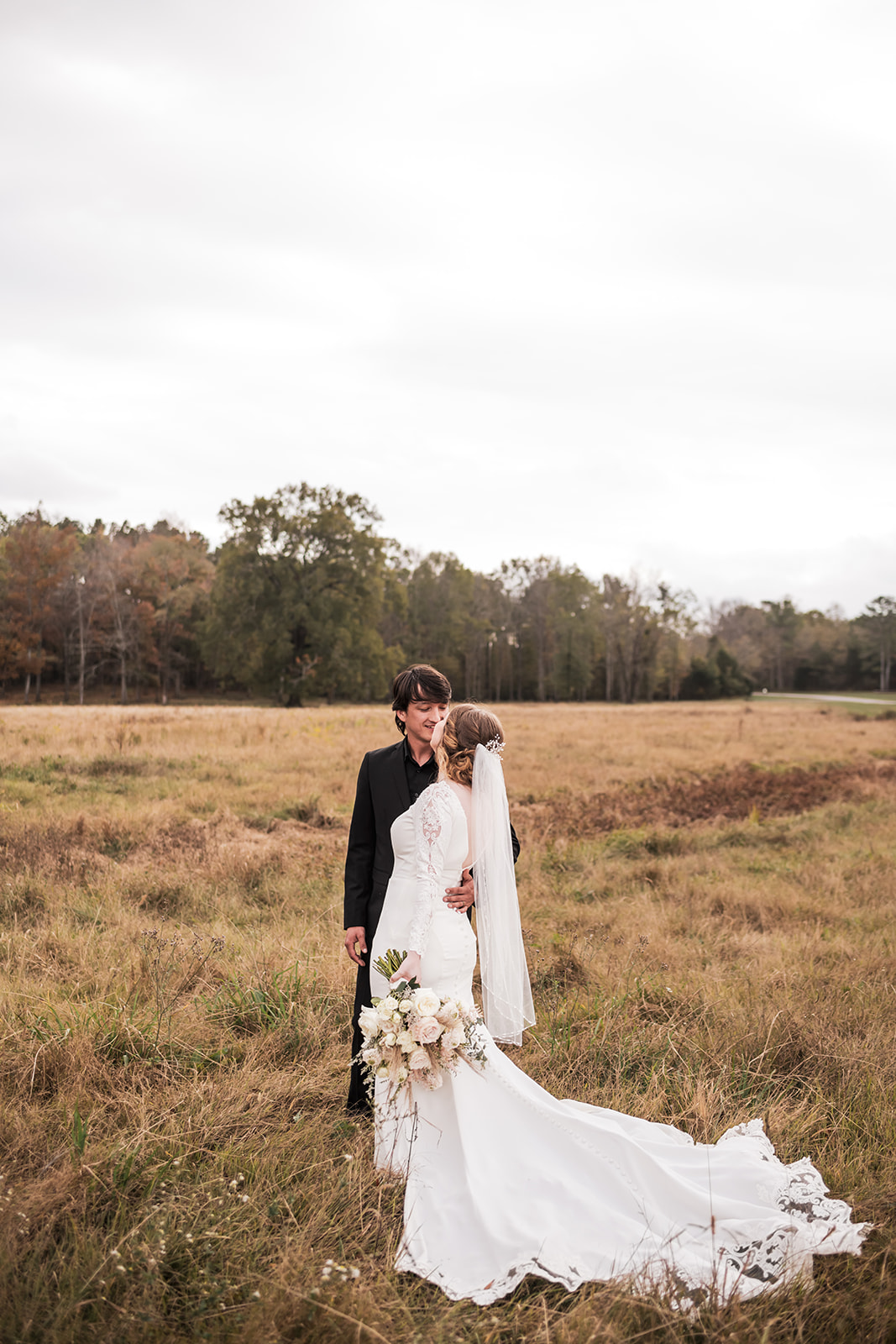 Isabelle & Alex lean close in a golden field at Covey Creek, her lace train fanned across the tall grass.
