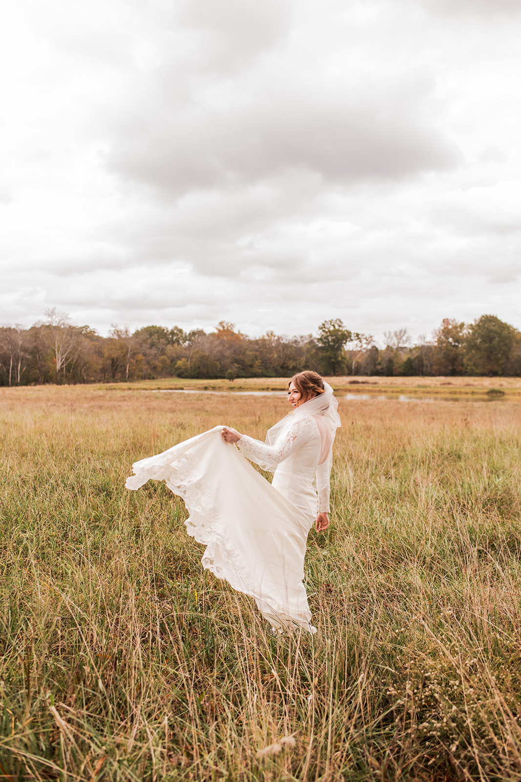 Isabelle looks back smiling in her lace train across a meadow at Covey Creek for Isabelle & Alex’s day.