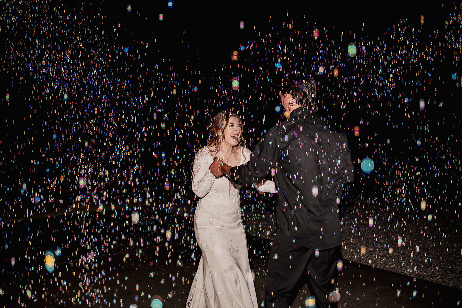 Isabelle & Alex laugh while dancing outdoors at night amid colorful bubbles at Covey Creek.