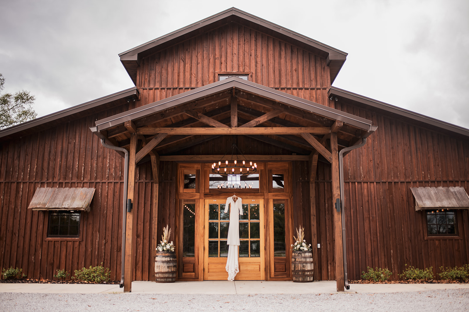 White lace wedding dress hangs in the Covey Creek barn doorway with barrel florals for Isabelle & Alex.