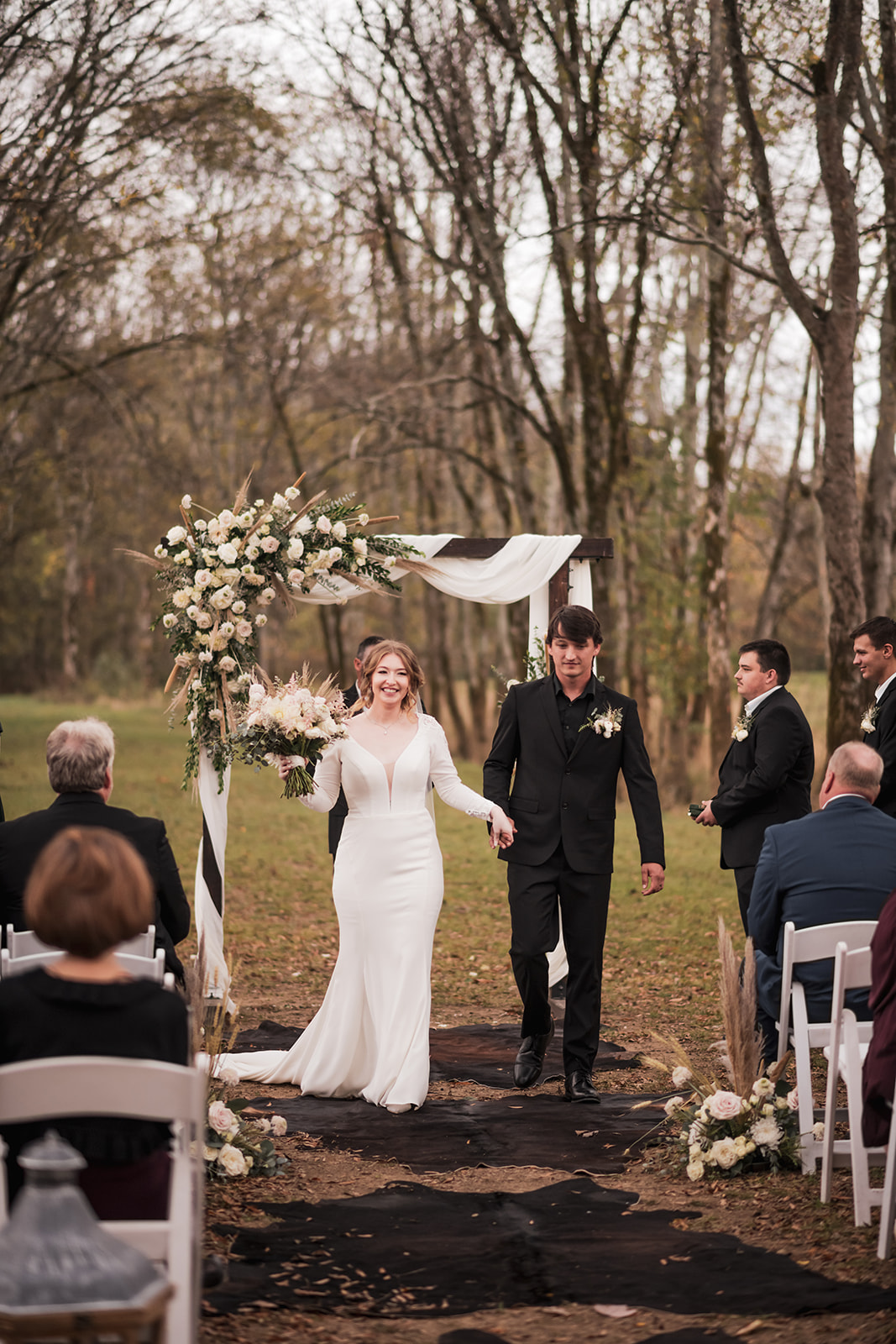 Isabelle & Alex smile walking the Tunnel of Love aisle at Covey Creek, floral wooden arch behind them.