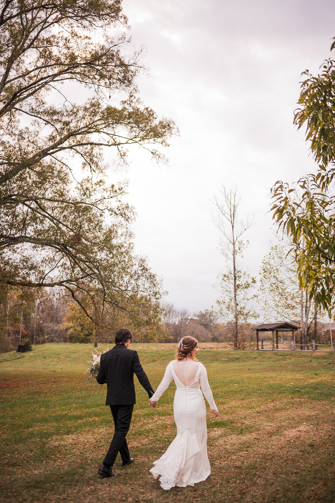 Isabelle & Alex walk hand in hand across a grassy field at Covey Creek, her open-back lace gown trailing.