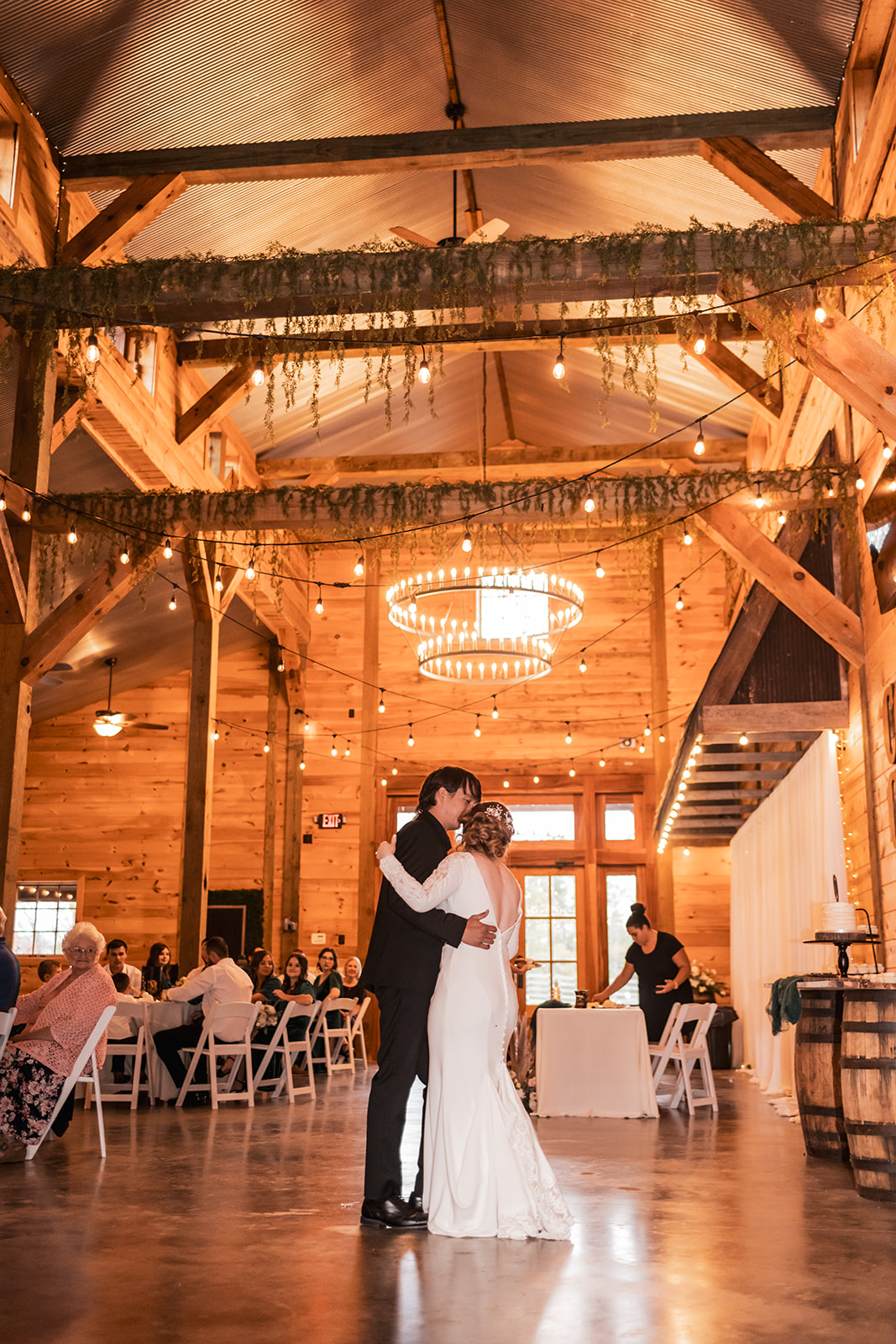 Alex kisses Isabelle’s forehead during their first dance under barn string lights at Covey Creek.