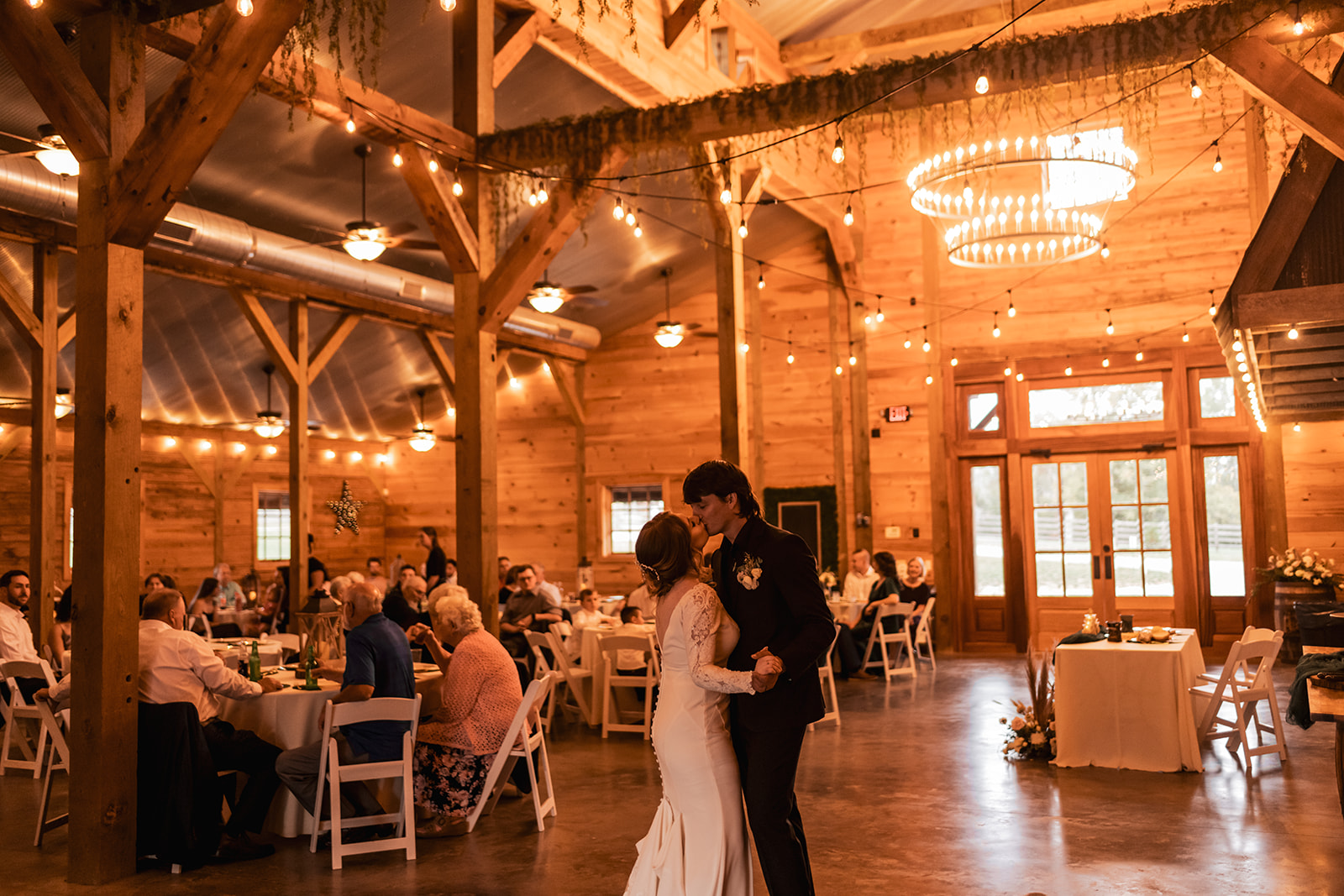 Isabelle & Alex kiss while slow dancing under string lights in the Covey Creek barn reception hall.
