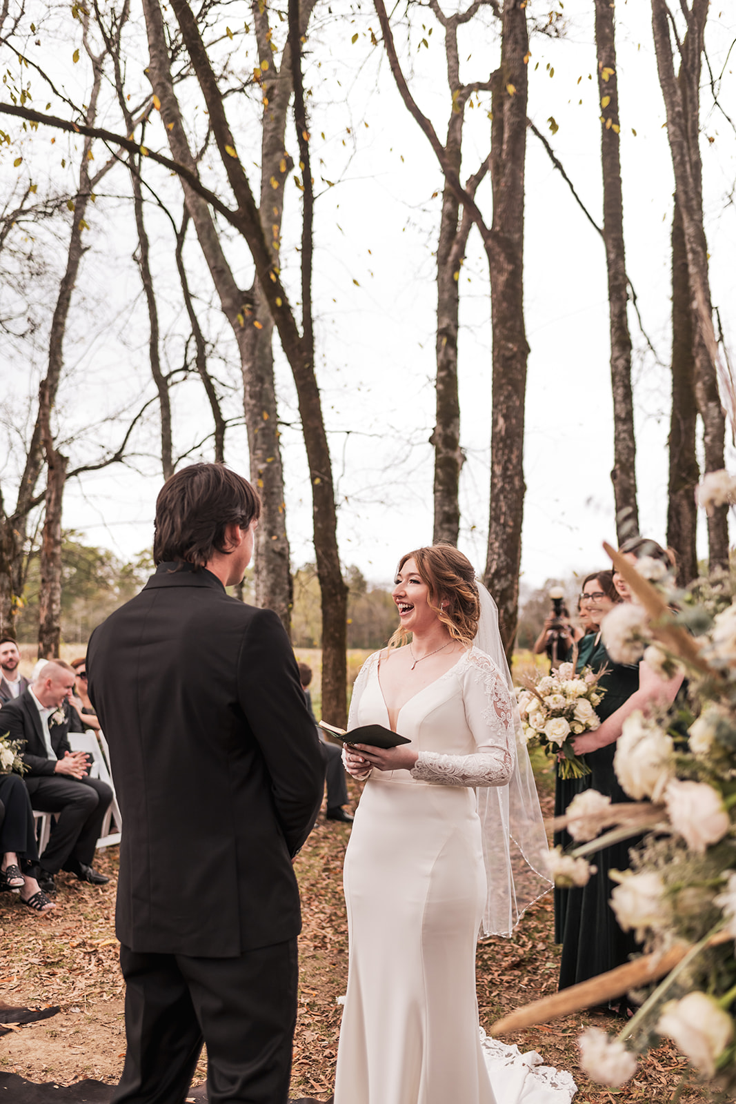 Isabelle laughs during vows facing Alex under autumn trees at their Covey Creek Tunnel of Love ceremony.