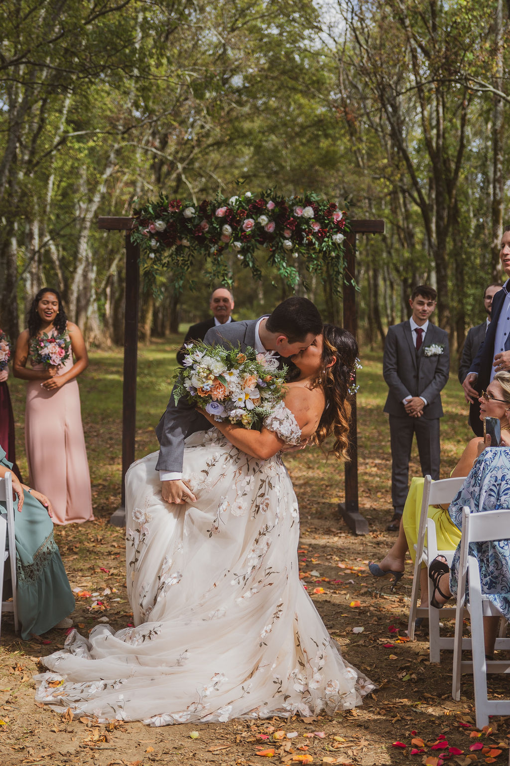 Jen & Alec share a dip kiss under the floral arbor as guests cheer in the Tunnel of Love at Covey Creek