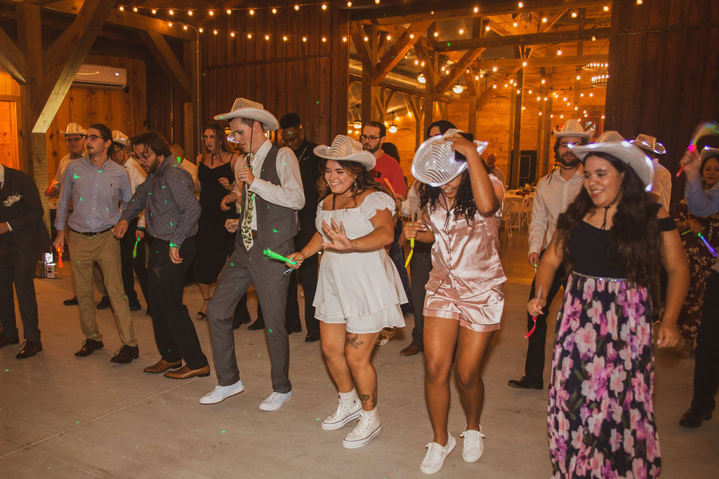 Jen & Alec dance with guests in glowing LED cowboy hats on the barn dance floor at Covey Creek