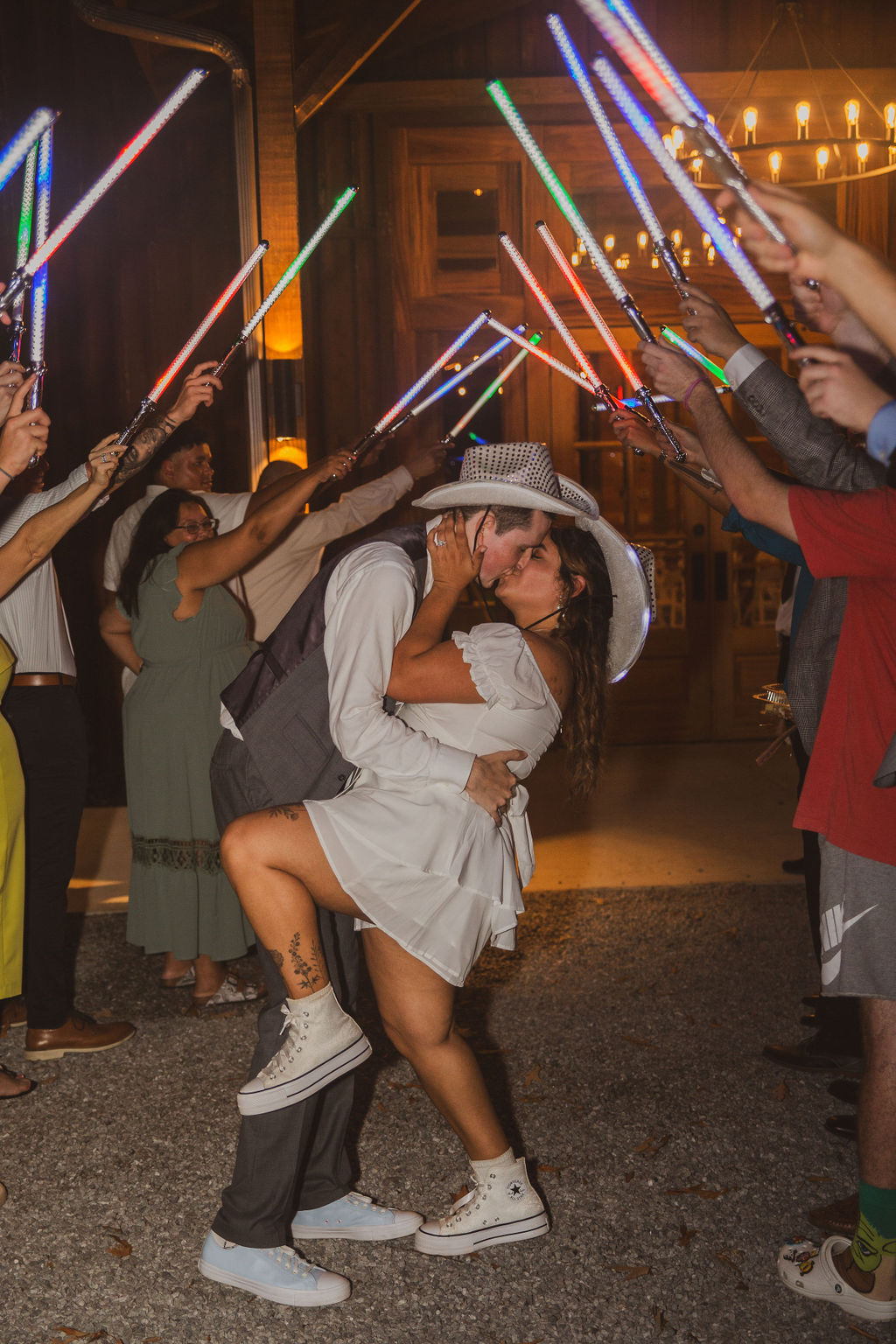 Jen & Alec kiss through a glowing lightsaber send-off tunnel in cowboy hats outside Covey Creek