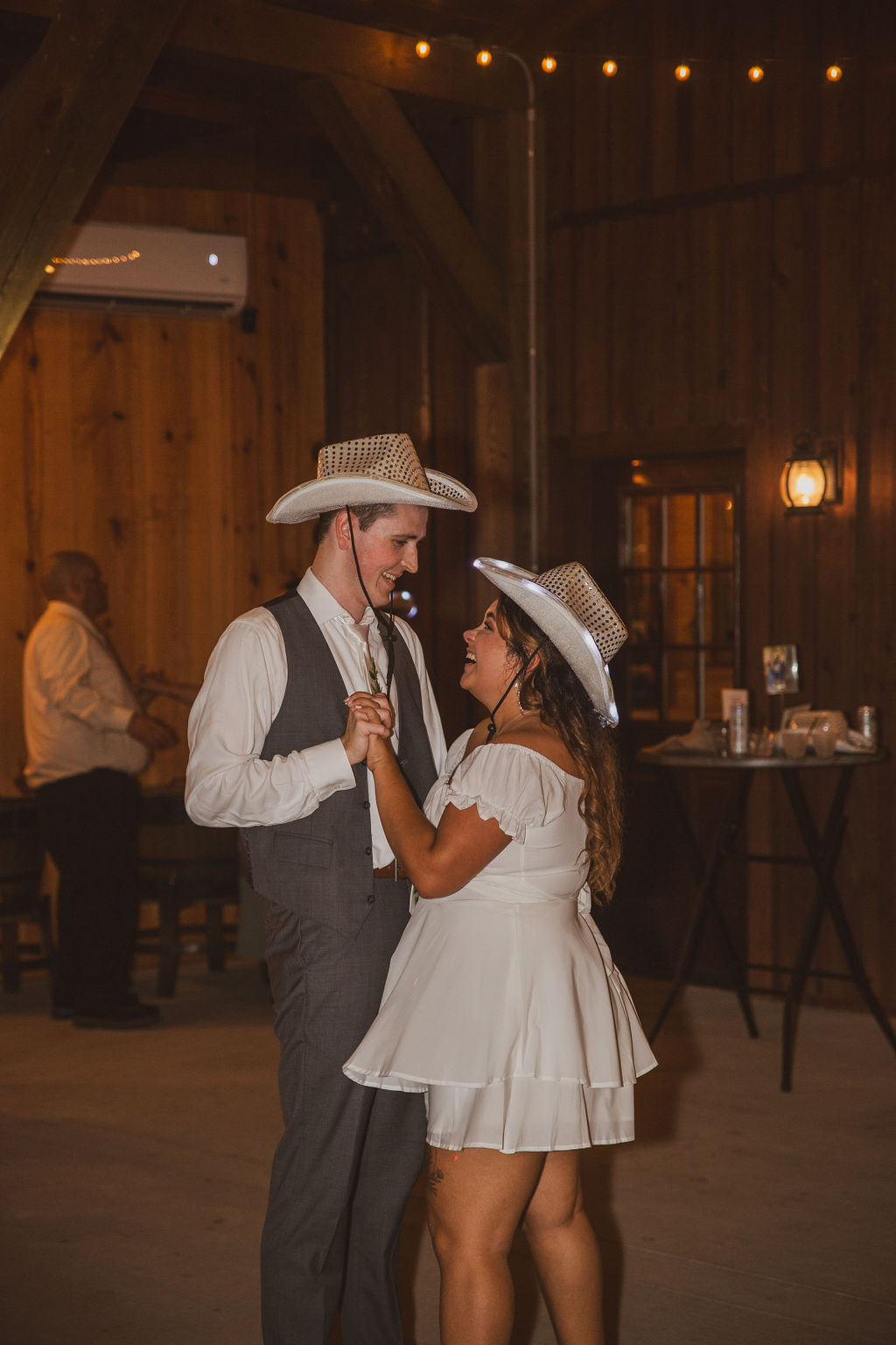 Jen & Alec laugh dancing in matching LED cowboy hats inside the barn reception at Covey Creek