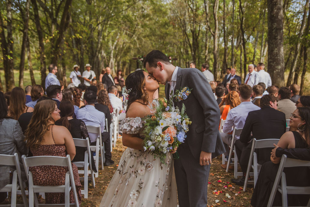 Jen & Alec kiss in the petal aisle as guests watch their Tunnel of Love ceremony at Covey Creek