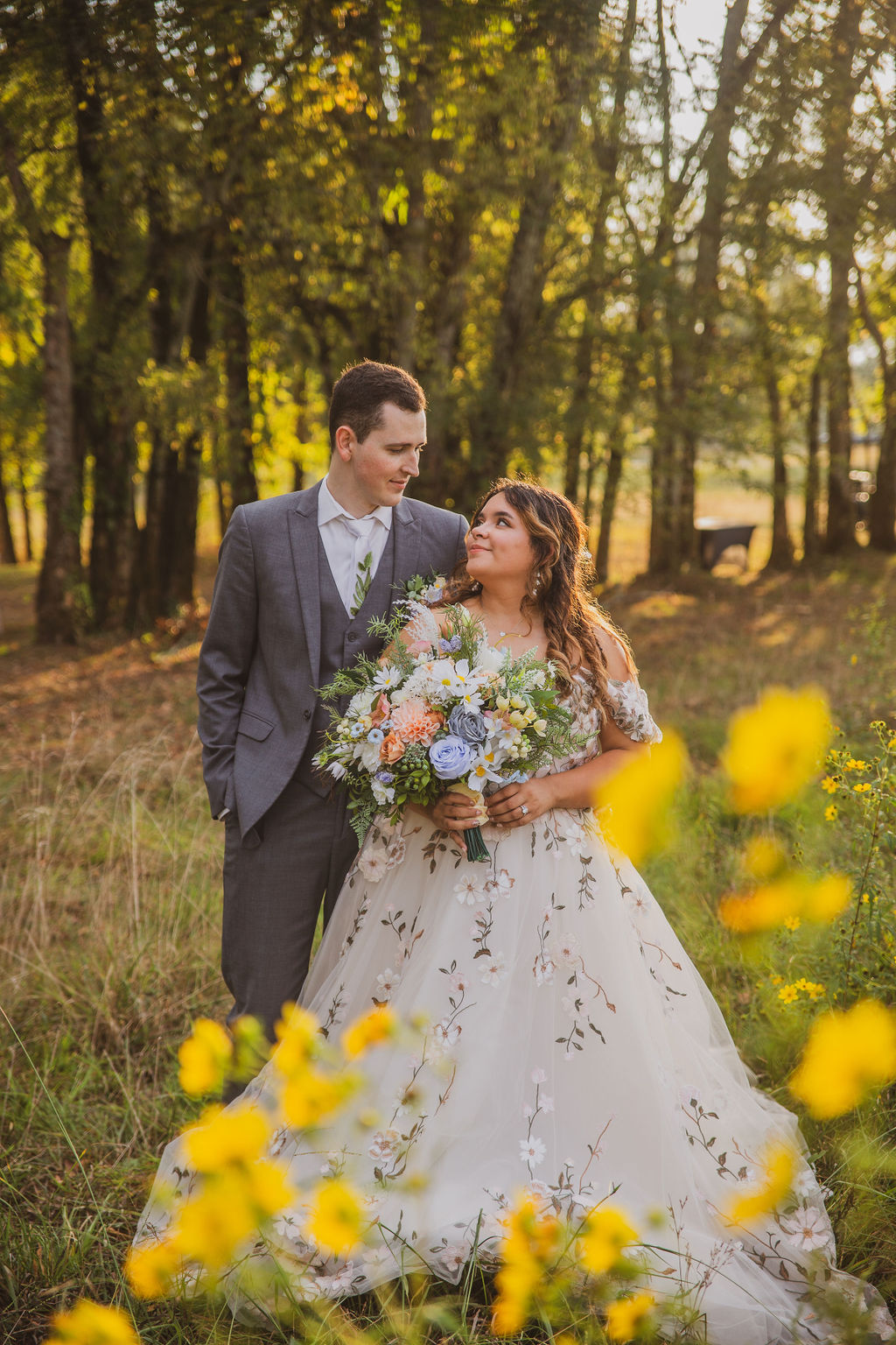 Jen & Alec share a glance among yellow wildflowers, her floral gown and bouquet bright at Covey Creek