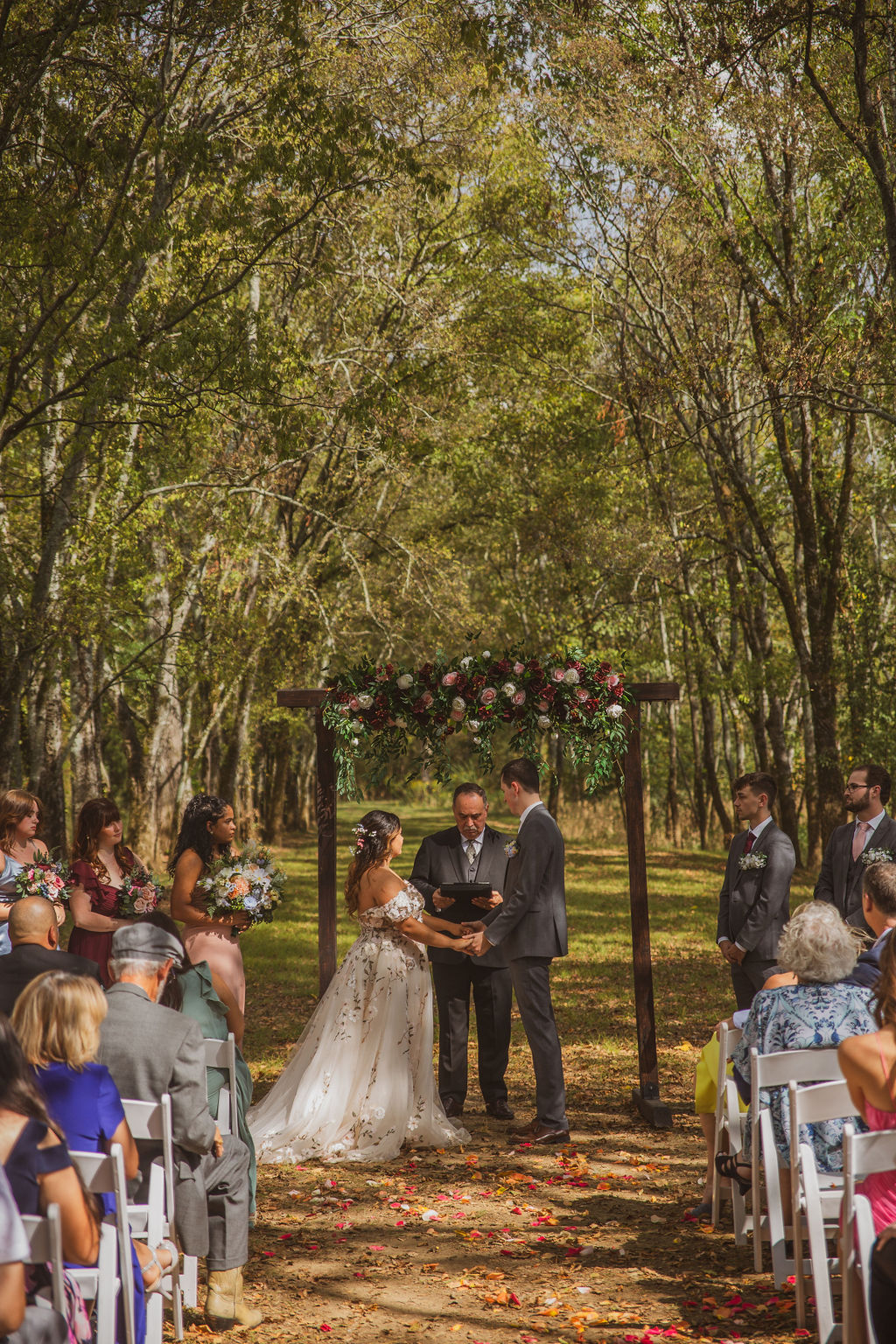 Seated guests watch Jen & Alec wed under a floral arbor in the Tunnel of Love at Covey Creek