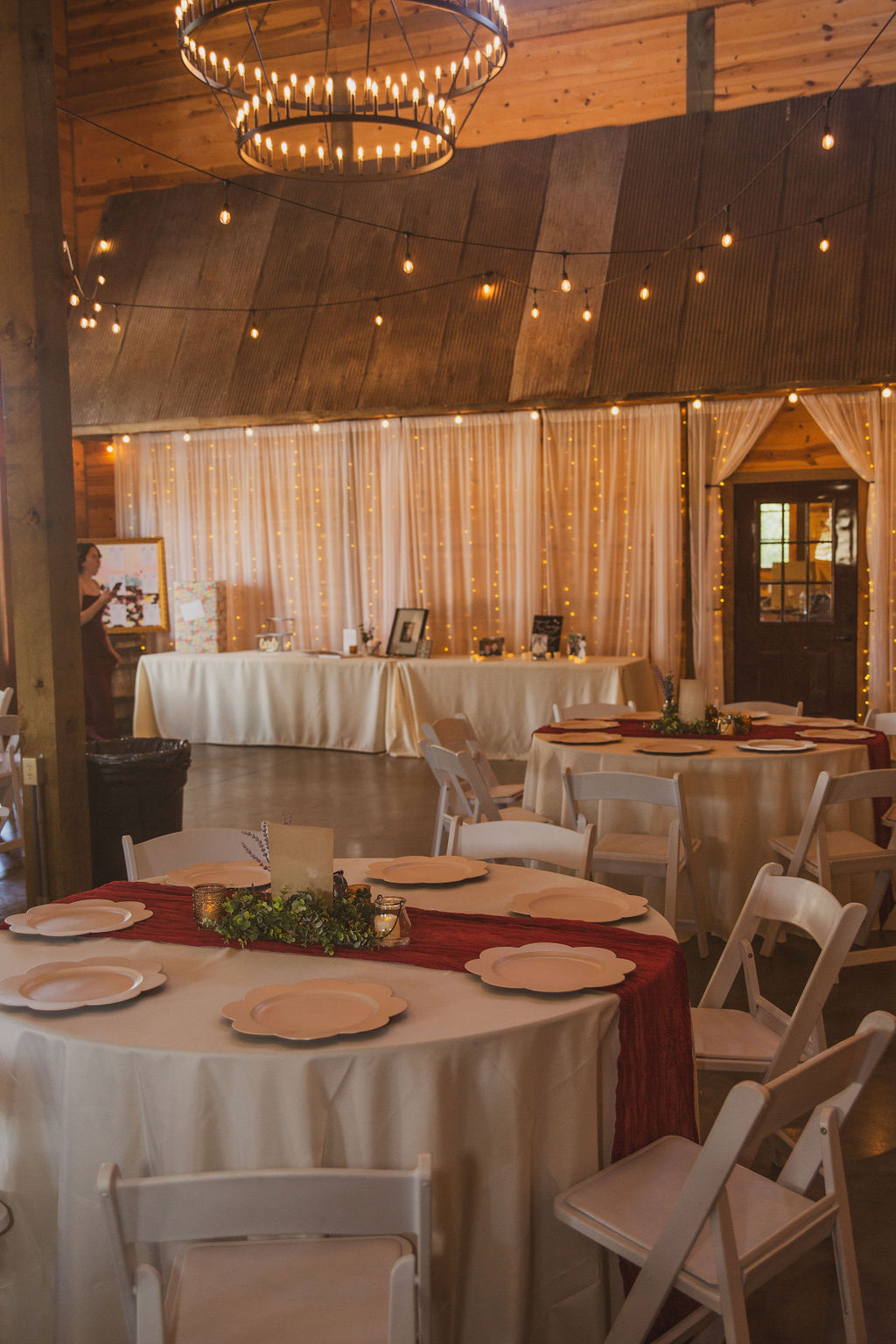 Round guest tables with greenery and string lights fill the barn reception hall for Jen & Alec at Covey Creek