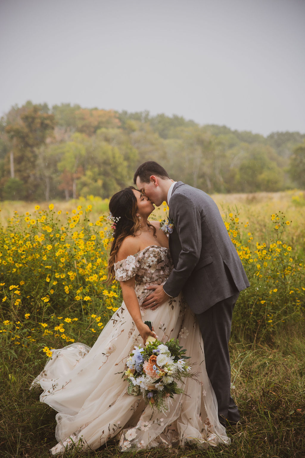 Jen & Alec kiss in a field of yellow wildflowers, her embroidered gown and bouquet at Covey Creek